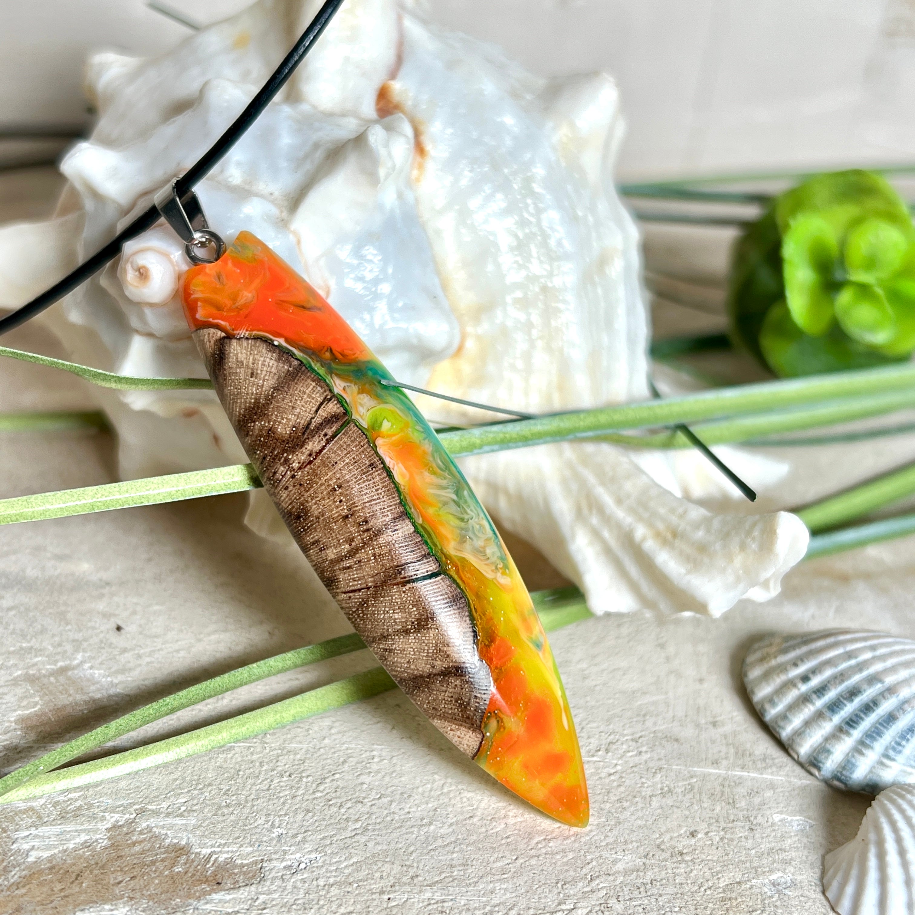 Handgefertigte Halskette „Tropical Glow“ mit Surfbrett-Anhänger aus naturbelassenem Rebholz (Weinrebe) und marmoriertem Epoxidharz in Grün, Orange, Türkis und Weiß. Größe des Anhängers ca. 6,5 × 2 cm. Das Harz fluoresziert eindrucksvoll unter UV-/Schwarzlicht. Edelstahl-Anhängerschlaufe, schwarze Lederkette (45 cm + 5 cm Verlängerung) mit Edelstahl-Karabiner. Unikat in maritim-sommerlichem Stil, ideal als besonderes Geschenk.
