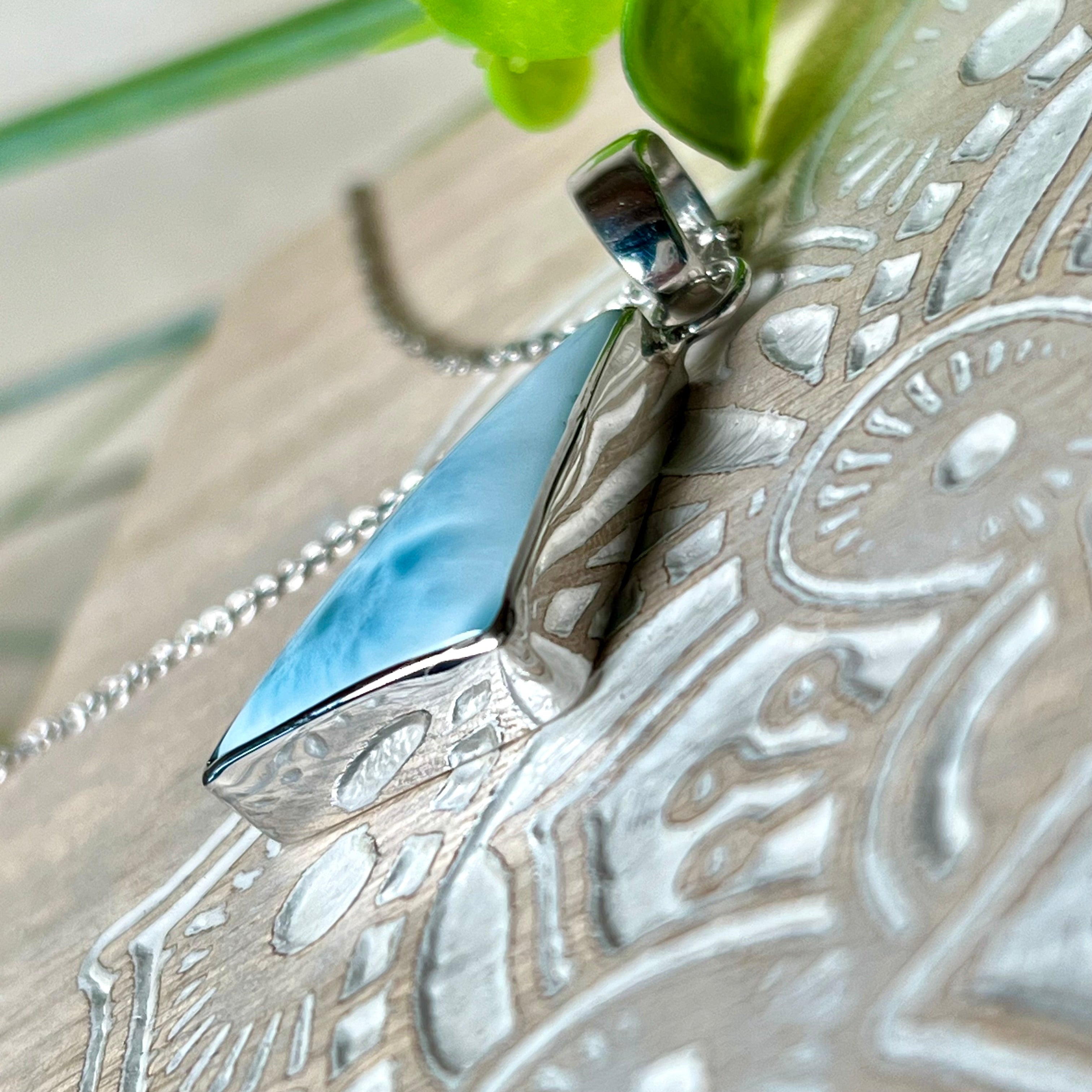 Larimar Anhänger in markanter Dreiecksform, eingefasst in rhodiniertes 925 Sterling Silber, vor strukturiertem Hintergrund mit grünen Blättern – stilvoller Edelsteinschmuck mit karibischem Flair.