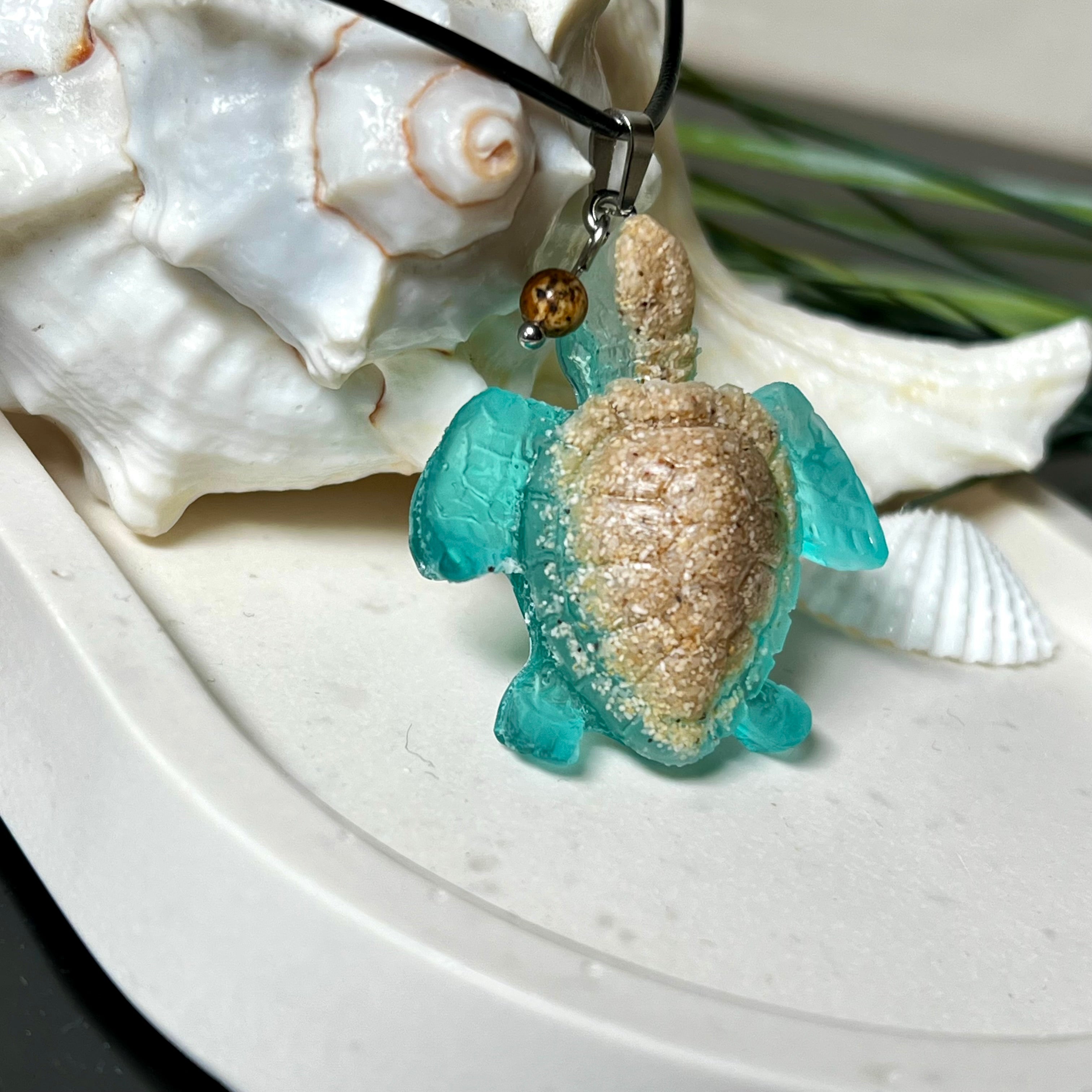 Handgefertigter Schildkröten-Anhänger Turtle Harmony aus echtem Meersand und transparent-türkisfarbenem Harz, kombiniert mit einer kleinen Jaspisperle. Symbol für Weisheit, Schutz und Harmonie. Mit Edelstahl-Anhängerschlaufe und Lederkette (45 + 5 cm). Maritimer Schmuck als Unikat, ideal als liebevolles Geschenk oder stilvolles Accessoire für den Alltag.