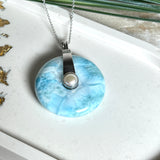 Echter Larimar-Donut (42 mm) mit Süßwasserperle, gefasst in rhodiniertem 925 Sterlingsilber. Mit 45 cm langer, rhodinierter Silberkette. Selten, edel & handgefertigt – inspiriert vom Blau der Karibik.