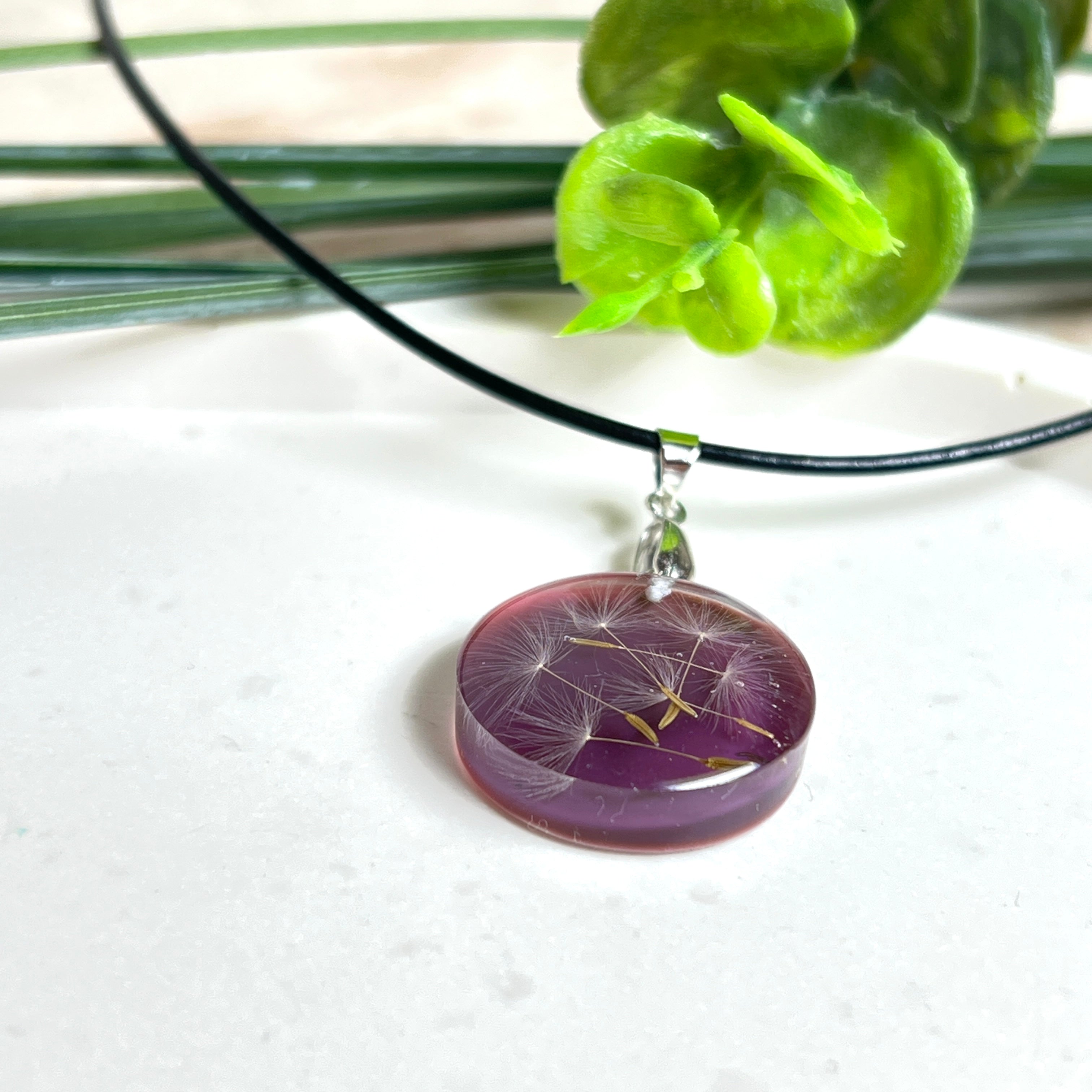 Runder Pusteblumen-Anhänger aus Harz, Hintergrund Brombeerfarben. Durchmesser 22 mm, Edelstahlöse, Lederkette verstellbar mit Edelstahlverschluss.