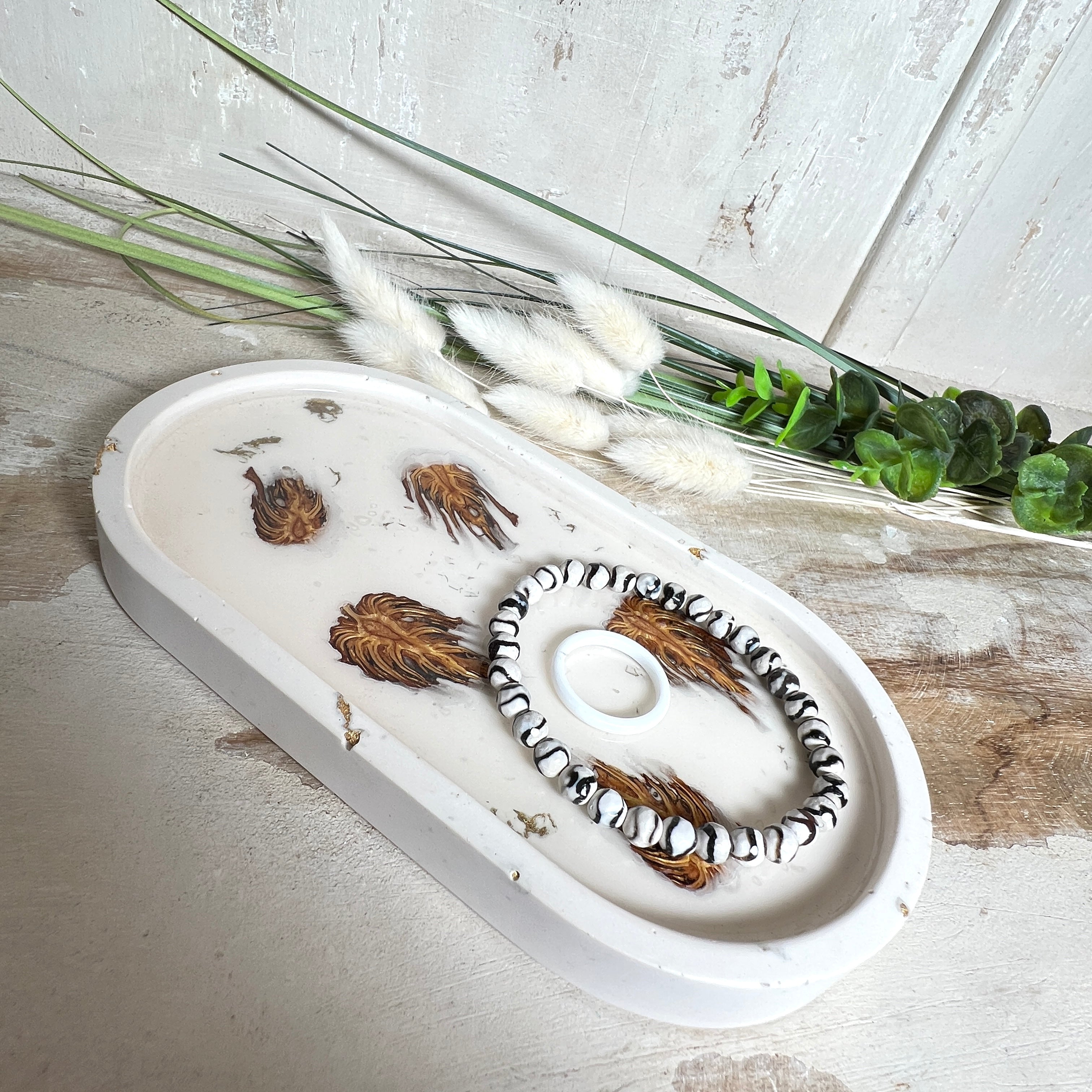 Handgefertigtes Schmucktablett aus Jesmonite mit echten Zapfen, die in einer glänzenden Resin-Schicht eingebettet sind. Die ovale Form und die natürliche Farbgebung machen es zu einem stilvollen Wohnaccessoire. Mit rutschfesten Korkpunkten auf der Unterseite ideal als Ablage für Schmuck, Schlüssel oder Dekoartikel. Jeder Artikel ist ein Unikat aus Handarbeit – Lieferung ohne Dekoration.