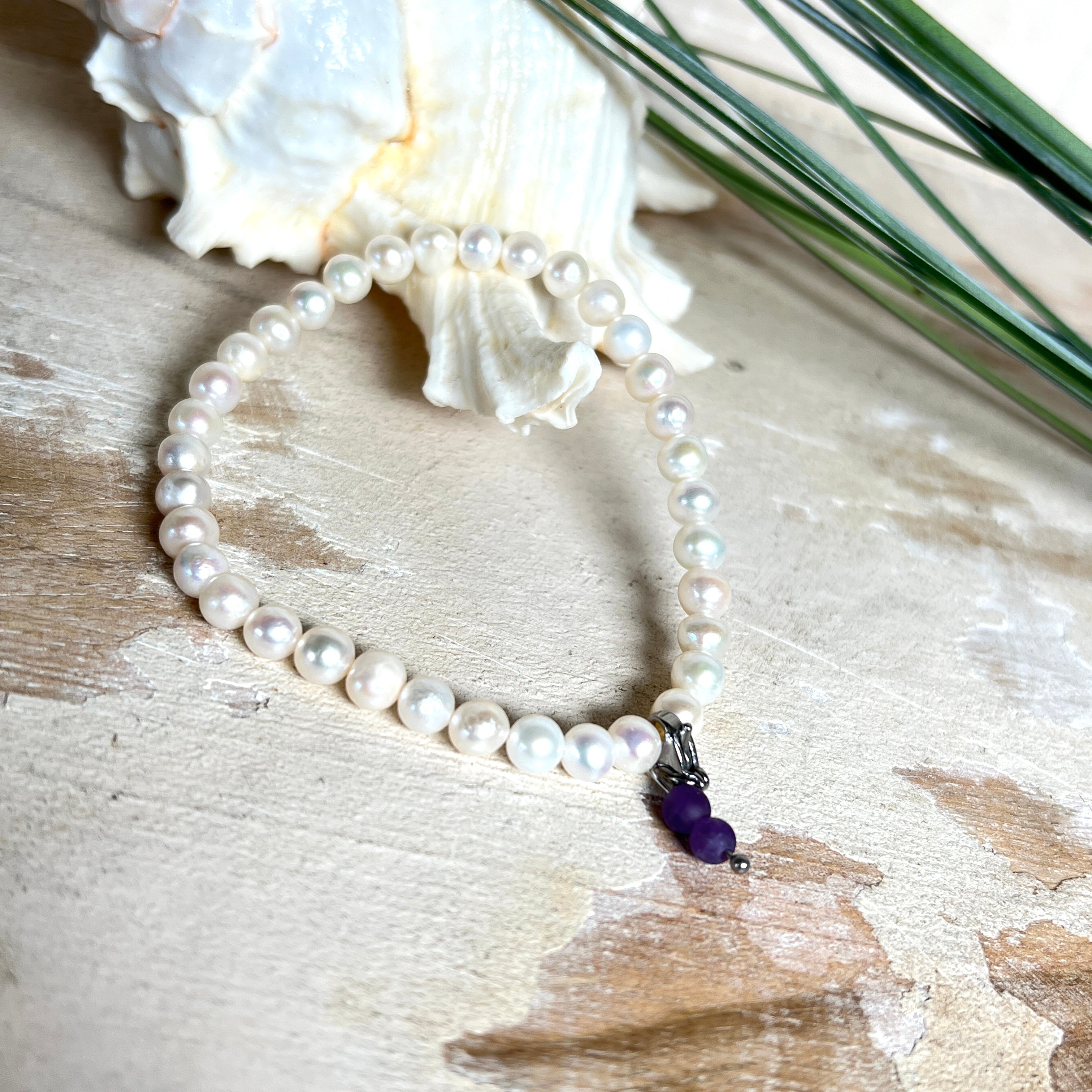 Handgefertigtes Armband „Sea Harmony“ mit schimmernden Süßwasserperlen (Ø ca. 6–7 mm), jede Perle ein Unikat. Auf elastischem Band gefädelt, mit einem filigranen Charmanhänger aus Amethyst-Perlen, befestigt an einem robusten Edelstahl-Karabiner. Ein Schmuckstück voller Eleganz, maritimer Harmonie und symbolischer Tiefe – ideal als Geschenk oder als stilvolles Accessoire.