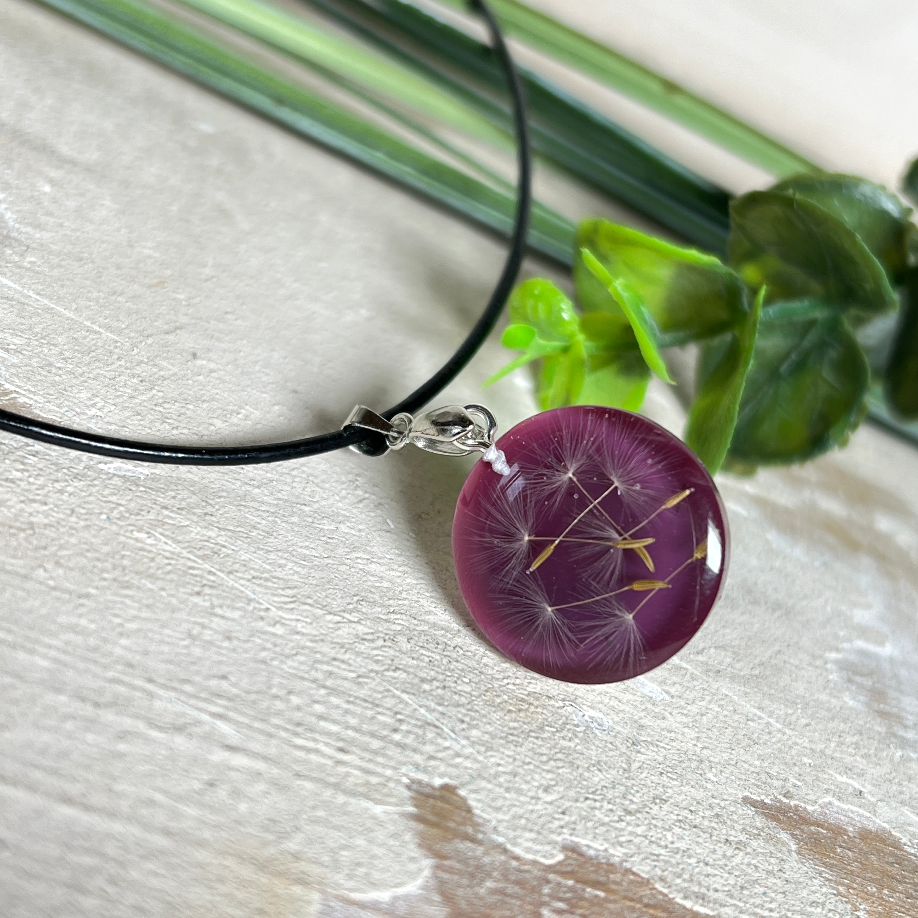 Runder Pusteblumen-Anhänger aus Harz, Hintergrund Brombeerfarben. Durchmesser 22 mm, Edelstahlöse, Lederkette verstellbar mit Edelstahlverschluss.