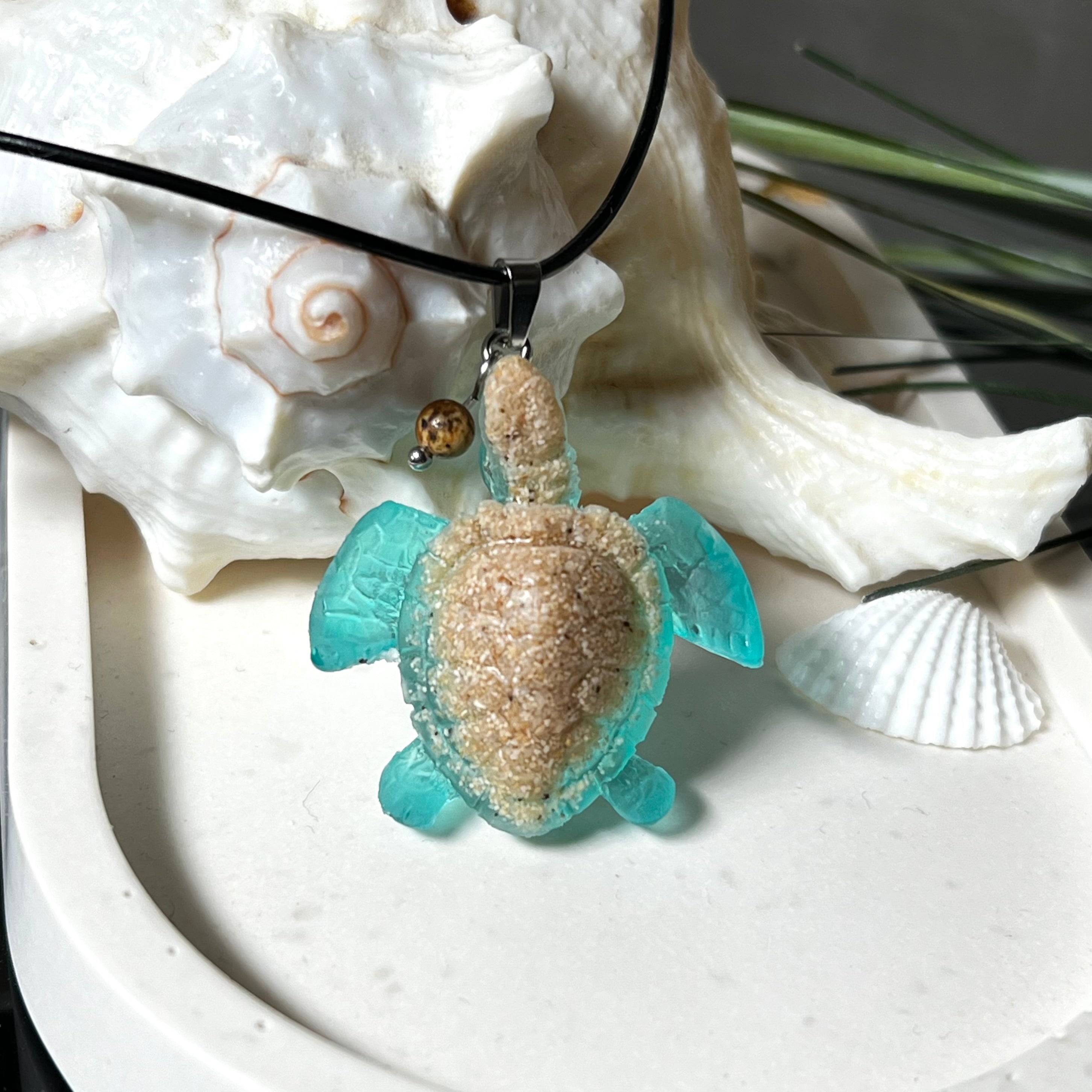 Handgefertigter Schildkröten-Anhänger Turtle Harmony aus echtem Meersand und transparent-türkisfarbenem Harz, kombiniert mit einer kleinen Jaspisperle. Symbol für Weisheit, Schutz und Harmonie. Mit Edelstahl-Anhängerschlaufe und Lederkette (45 + 5 cm). Maritimer Schmuck als Unikat, ideal als liebevolles Geschenk oder stilvolles Accessoire für den Alltag.