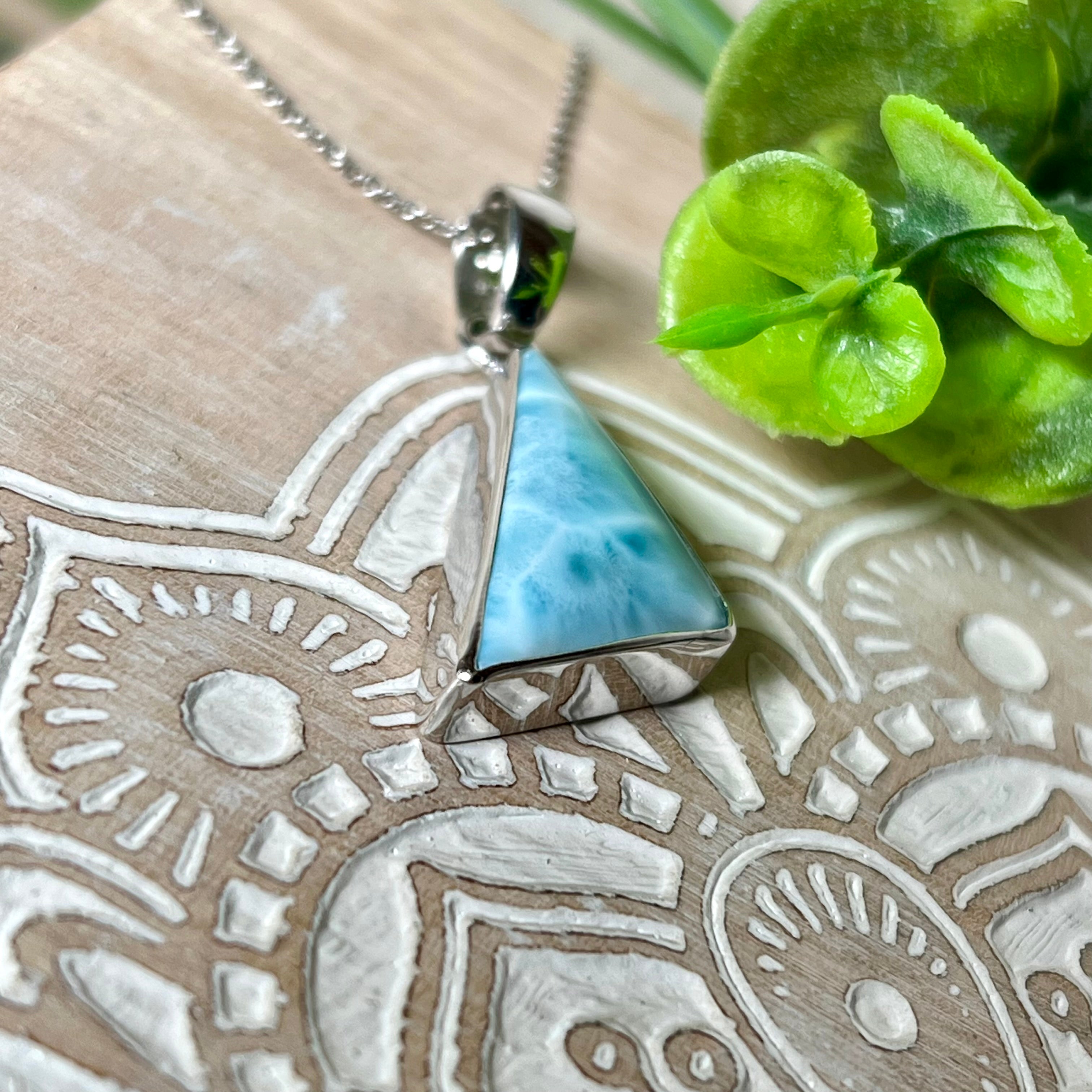 Larimar Anhänger in markanter Dreiecksform, eingefasst in rhodiniertes 925 Sterling Silber, vor strukturiertem Hintergrund mit grünen Blättern – stilvoller Edelsteinschmuck mit karibischem Flair.