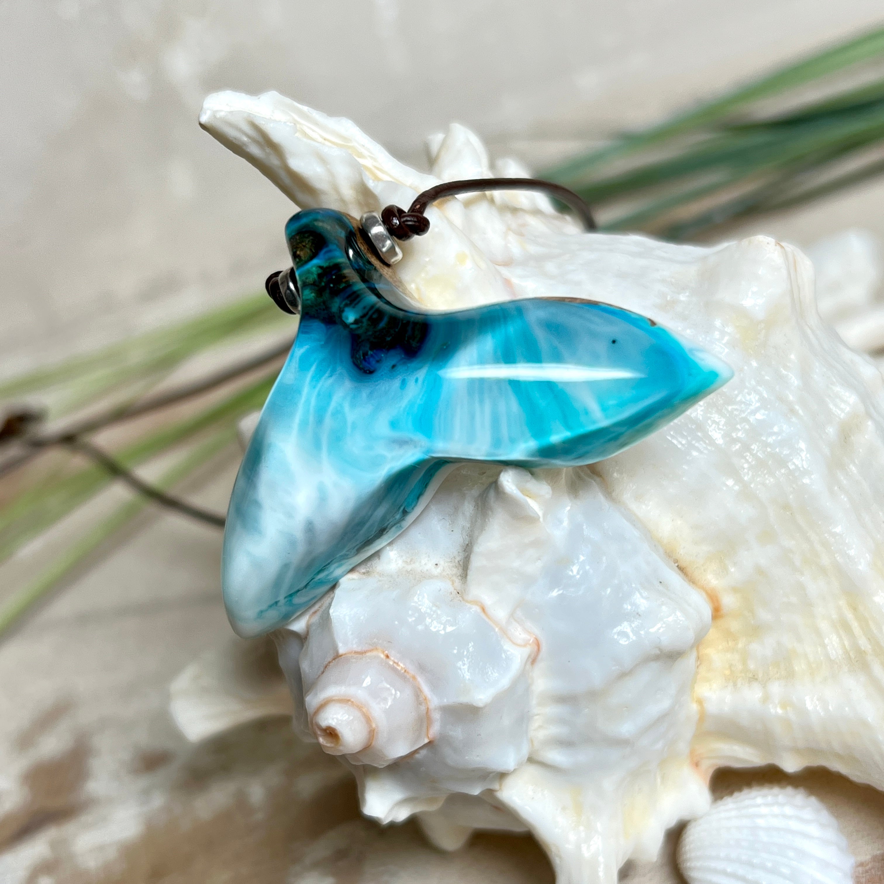 Walflossen-Anhänger „Flossenklang“ – handgefertigtes Unikat aus Maserholz und türkis-blau-grauen und weißem Harz. Die elegant geschwungene Form erinnert an die Flosse eines Wals und symbolisiert Freiheit, Stärke und Naturverbundenheit. Mit verstellbarem braunem Lederband gefertigt, ist jedes Stück ein individuelles Schmuckstück für Meeresliebhaber und Natursuchende. Maritimer Halsschmuck, inspiriert vom Ozean, glatt poliert und mit Liebe zum Detail von Hand gearbeitet.