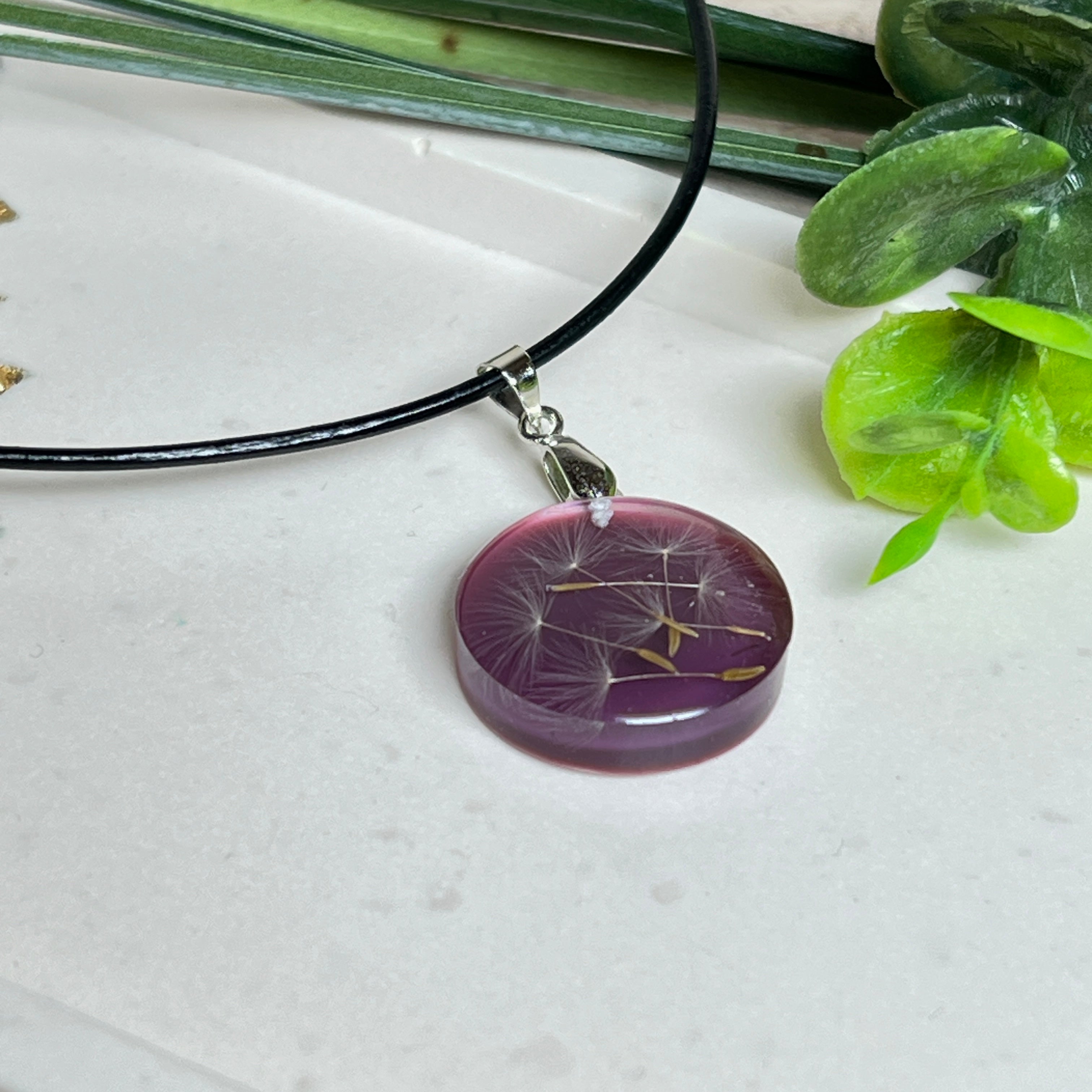 Runder Pusteblumen-Anhänger aus Harz, Hintergrund Brombeerfarben. Durchmesser 22 mm, Edelstahlöse, Lederkette verstellbar mit Edelstahlverschluss.