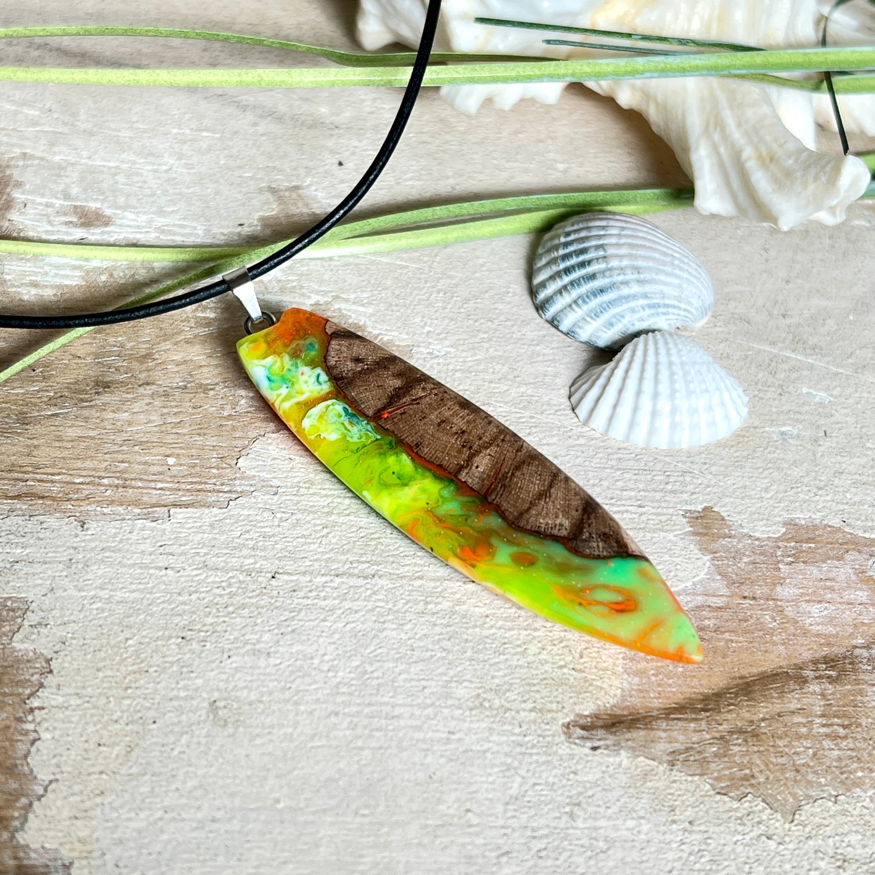 Handgefertigte Halskette „Tropical Glow“ mit Surfbrett-Anhänger aus naturbelassenem Rebholz (Weinrebe) und marmoriertem Epoxidharz in Grün, Orange, Türkis und Weiß. Größe des Anhängers ca. 6,5 × 2 cm. Das Harz fluoresziert eindrucksvoll unter UV-/Schwarzlicht. Edelstahl-Anhängerschlaufe, schwarze Lederkette (45 cm + 5 cm Verlängerung) mit Edelstahl-Karabiner. Unikat in maritim-sommerlichem Stil, ideal als besonderes Geschenk.