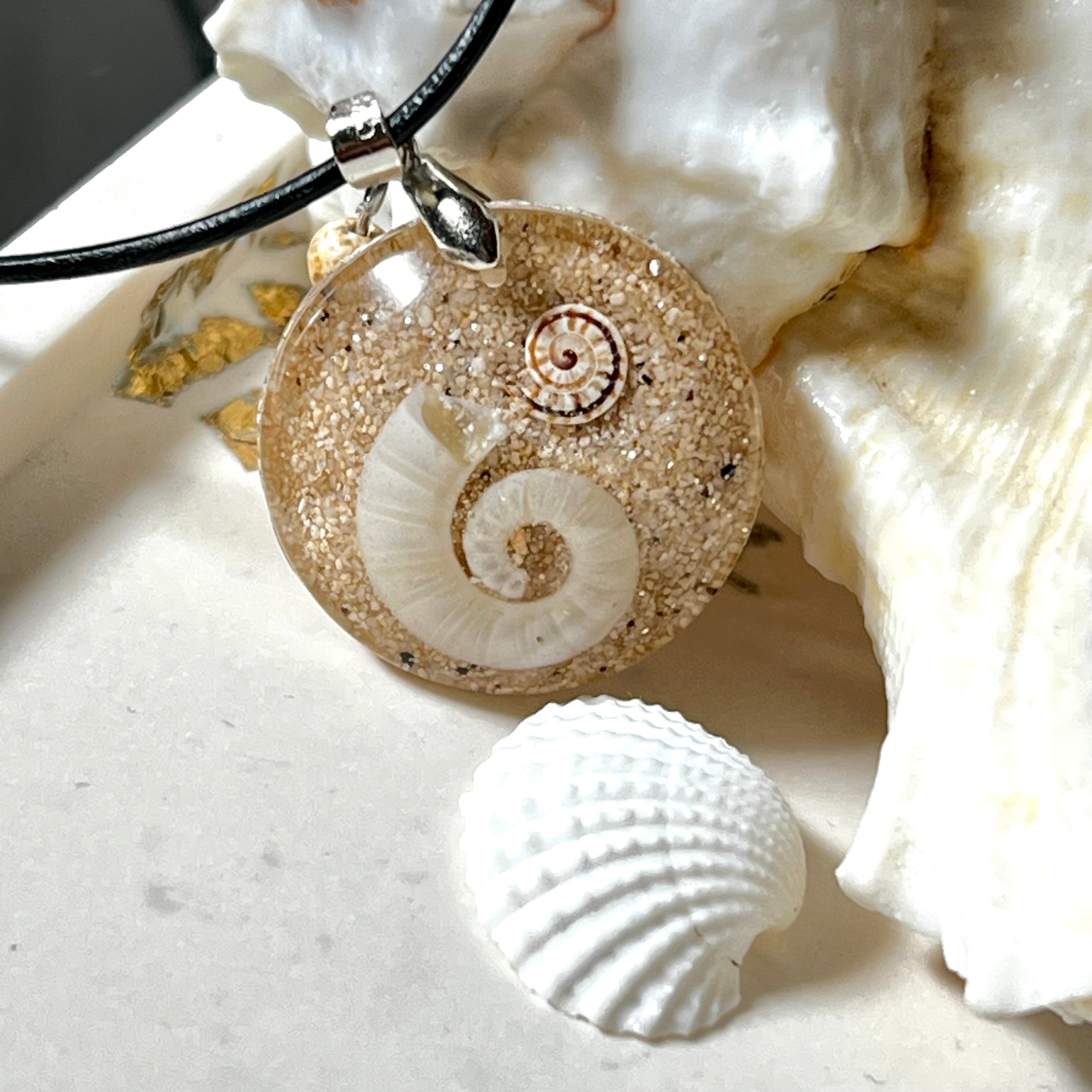 Handgemachter Anhänger mit echter Spirale, kleiner Schnecke, Meersand und feinem Glitzereffekt im Harz. Verziert mit einer Jaspisperle, Edelstahlöse und Lederkette mit Verlängerung. Maritimer Natur-Schmuck, inspiriert vom Ozean