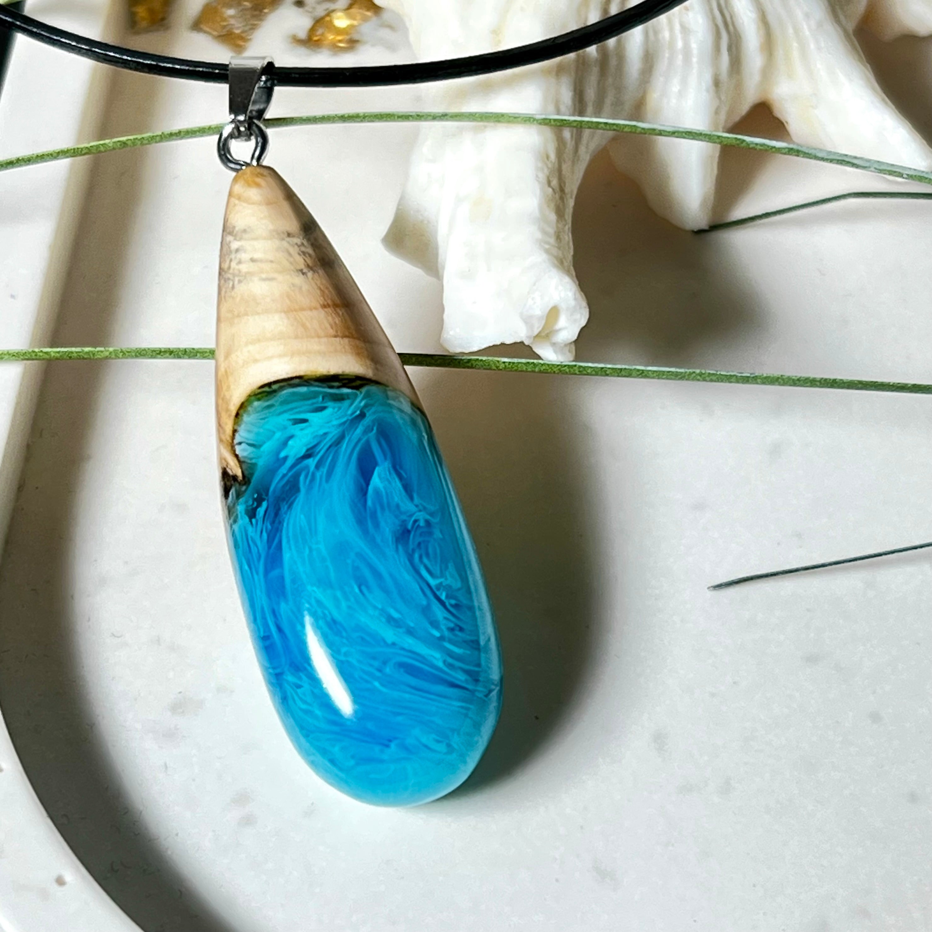 Tropfenförmiger Anhänger aus Maserholz und Harz in leuchtenden Blautönen und Weiß. Inspiriert vom Meer, in Handarbeit gegossen,gesägt, geschliffen und hochglanzpoliert. Mit verstellbarer Lederkette (45 + 5 cm) und Edelstahlkarabiner. Jeder Anhänger ist ein Unikat mit natürlicher Maserung. Ein maritimes Schmuckstück für Naturfreunde und alle, die das Wasser lieben.