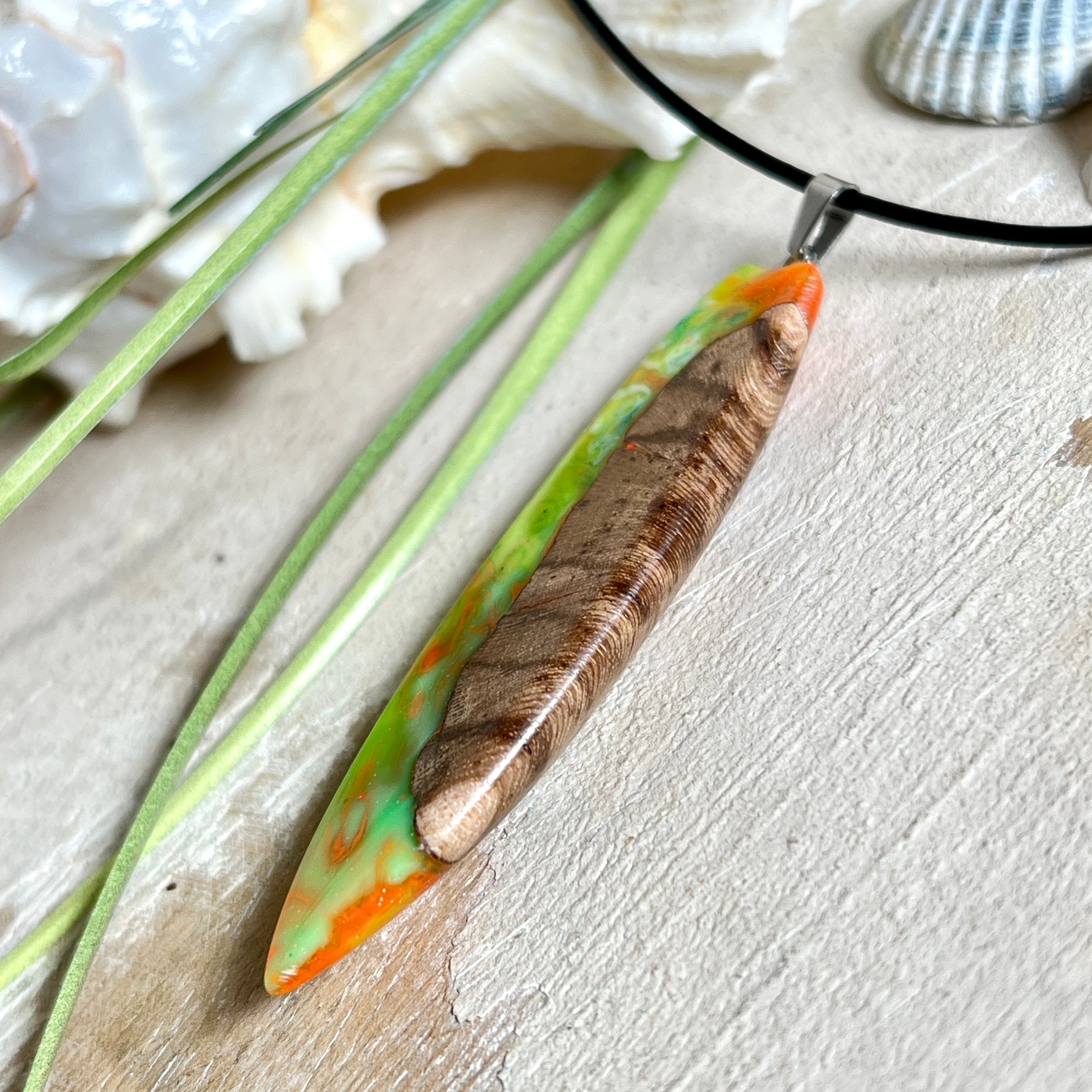 Handgefertigte Halskette „Tropical Glow“ mit Surfbrett-Anhänger aus naturbelassenem Rebholz (Weinrebe) und marmoriertem Epoxidharz in Grün, Orange, Türkis und Weiß. Größe des Anhängers ca. 6,5 × 2 cm. Das Harz fluoresziert eindrucksvoll unter UV-/Schwarzlicht. Edelstahl-Anhängerschlaufe, schwarze Lederkette (45 cm + 5 cm Verlängerung) mit Edelstahl-Karabiner. Unikat in maritim-sommerlichem Stil, ideal als besonderes Geschenk.