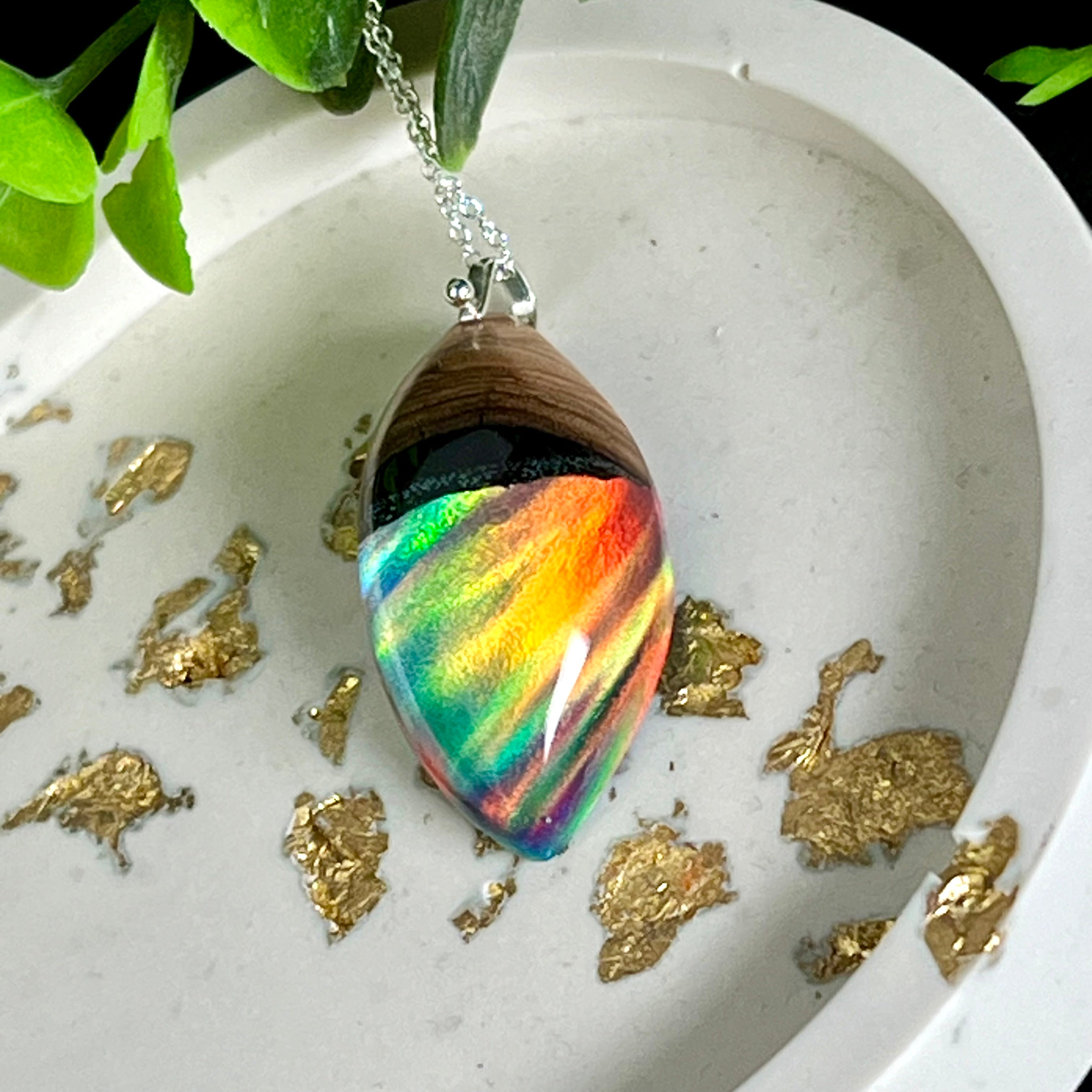 „Handgefertigter Anhänger aus Olivenholz, klarem Harz und schimmerndem Labor-Opal mit Aurora-Borealis-Effekt. Regenbogenfarben und einzigartige Maserung machen das Schmuckstück mit 925-Sterlingsilberkette zum perfekten Accessoire oder Geschenk.“