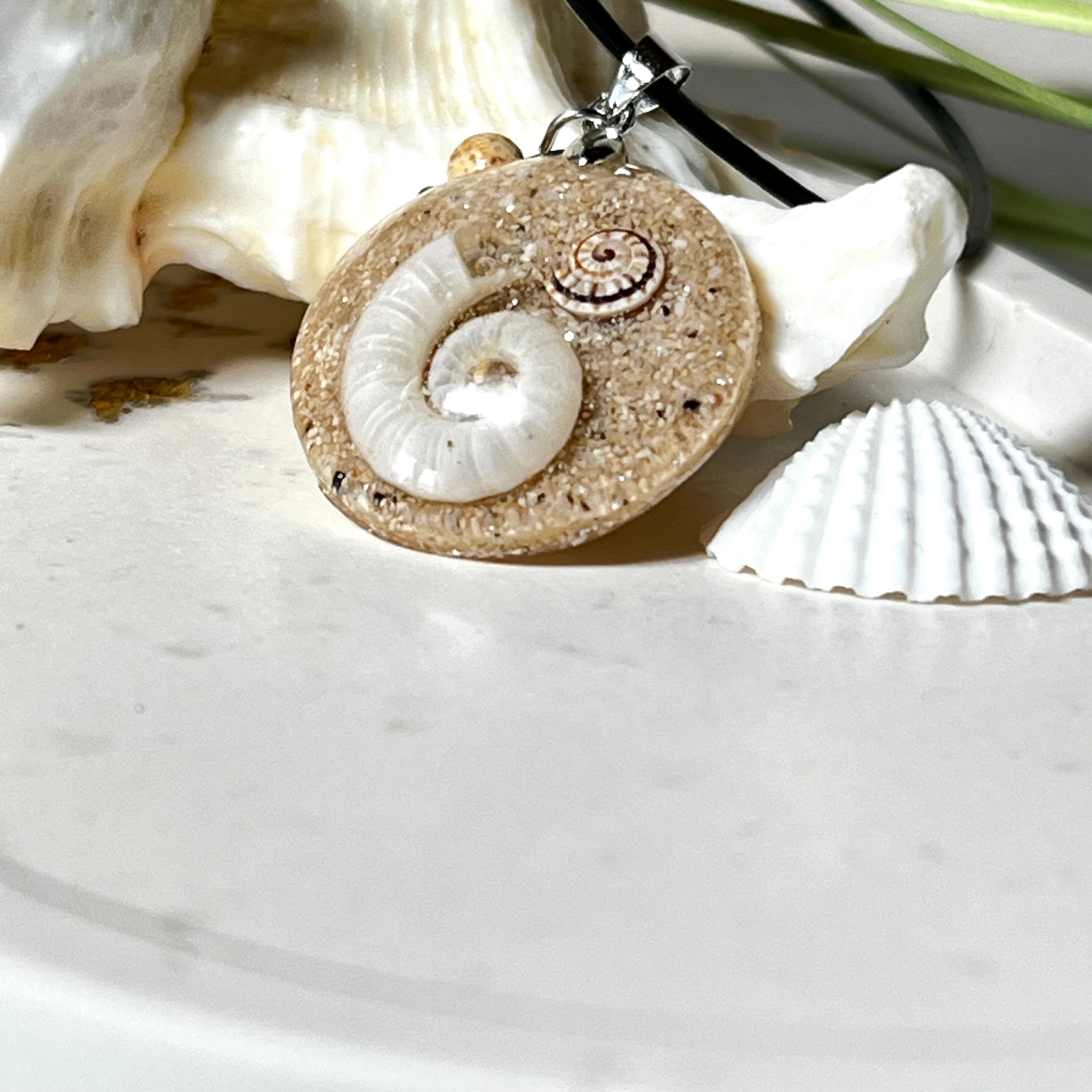 Handgemachter Anhänger mit echter Spirale, kleiner Schnecke, Meersand und feinem Glitzereffekt im Harz. Verziert mit einer Jaspisperle, Edelstahlöse und Lederkette mit Verlängerung. Maritimer Natur-Schmuck, inspiriert vom Ozean