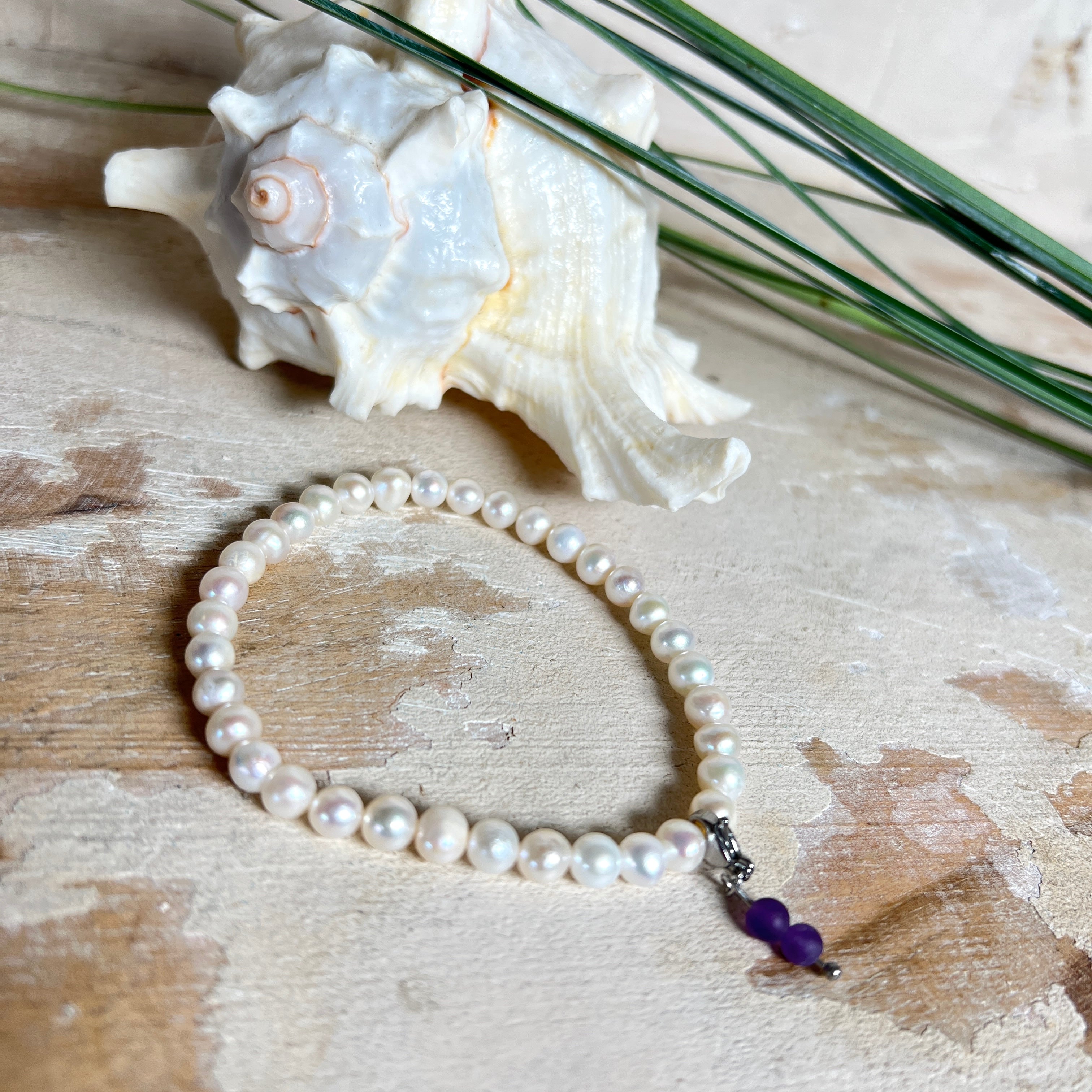 Handgefertigtes Armband „Sea Harmony“ mit schimmernden Süßwasserperlen (Ø ca. 6–7 mm), jede Perle ein Unikat. Auf elastischem Band gefädelt, mit einem filigranen Charmanhänger aus Amethyst-Perlen, befestigt an einem robusten Edelstahl-Karabiner. Ein Schmuckstück voller Eleganz, maritimer Harmonie und symbolischer Tiefe – ideal als Geschenk oder als stilvolles Accessoire.