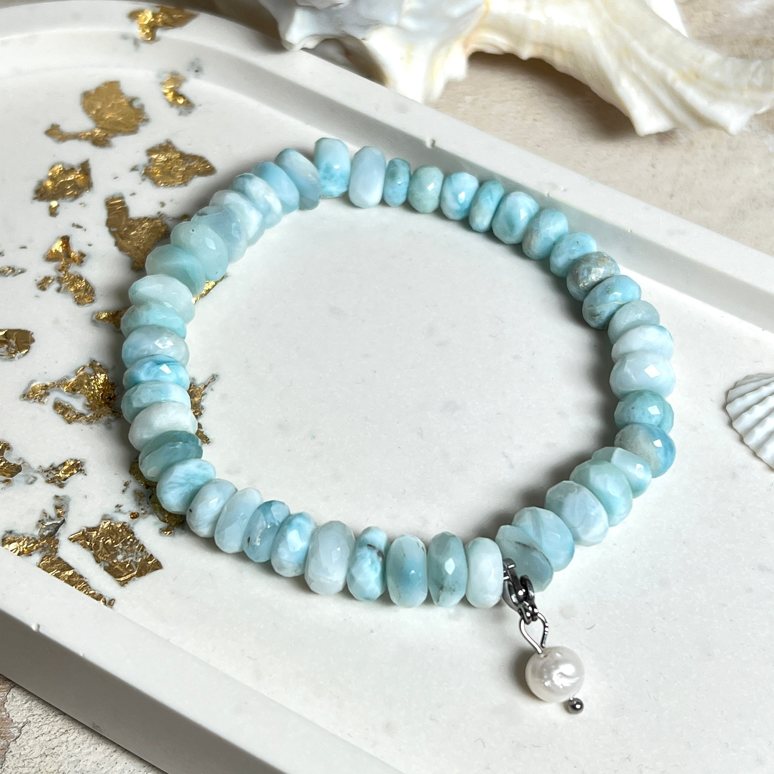 Handgefertigtes Armband aus seltenem Larimar mit facettierten, türkis-blauen Edelsteinperlen (Ø ca. 6–7 mm), elastischem Band und einem zarten Süßwasserperlen-Charm an Edelstahlkarabiner. Der wertvolle Larimar, auch „Stein des Atlantis“ genannt, gilt als Edelstein der Ruhe und Meeresverbundenheit.