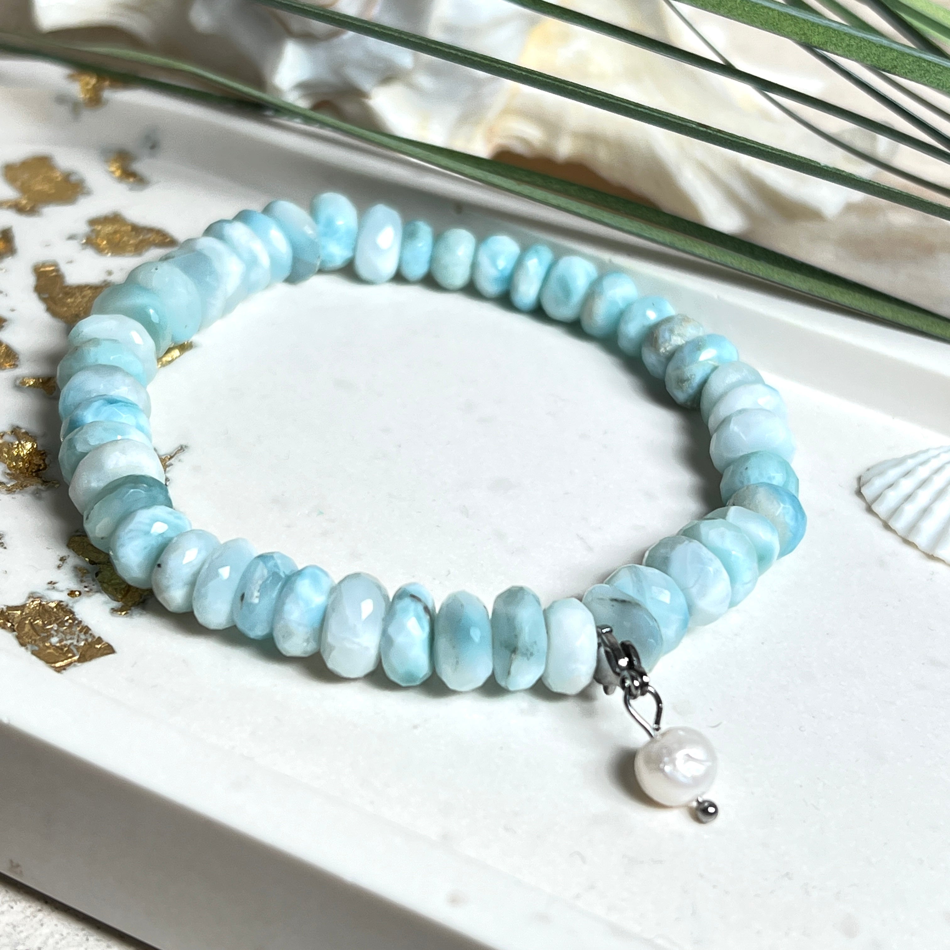 Handgefertigtes Armband aus seltenem Larimar mit facettierten, türkis-blauen Edelsteinperlen (Ø ca. 6–7 mm), elastischem Band und einem zarten Süßwasserperlen-Charm an Edelstahlkarabiner. Der wertvolle Larimar, auch „Stein des Atlantis“ genannt, gilt als Edelstein der Ruhe und Meeresverbundenheit.