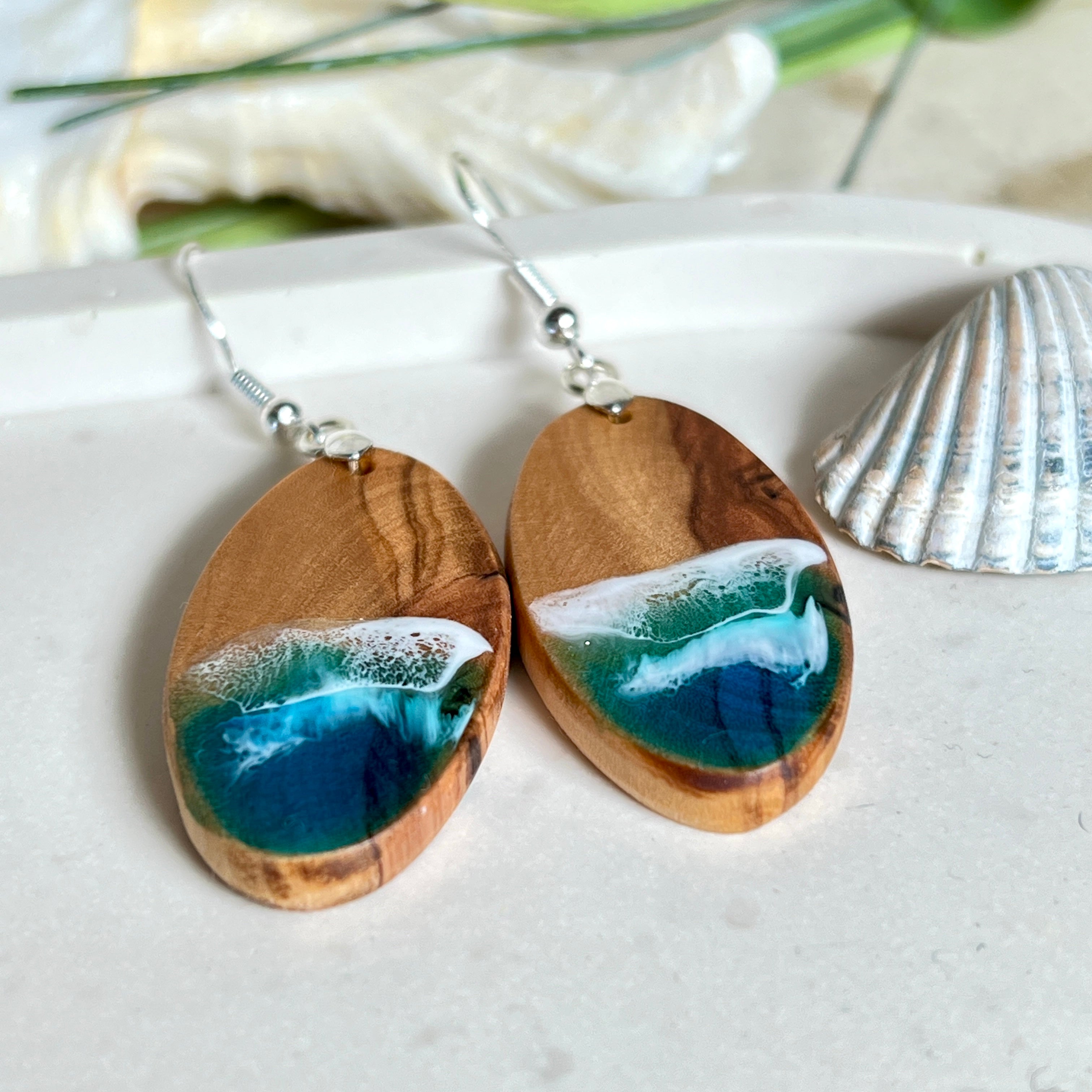 Handgefertigte Ohrringe „Wave Harmony“ aus Olivenholz und Epoxidharz in Blau-, Türkis- und Weißtönen. Das Design erinnert an Meereswellen am Strand. Jeder Ohrring ist ein Unikat mit individueller Maserung. Versilberte, nickelfreie und bleifreie Anhängerschlaufe, 925 Silber Ohrhaken. Maritimer Schmuck – perfekt für Meerliebhaber und als edles Geschenk.