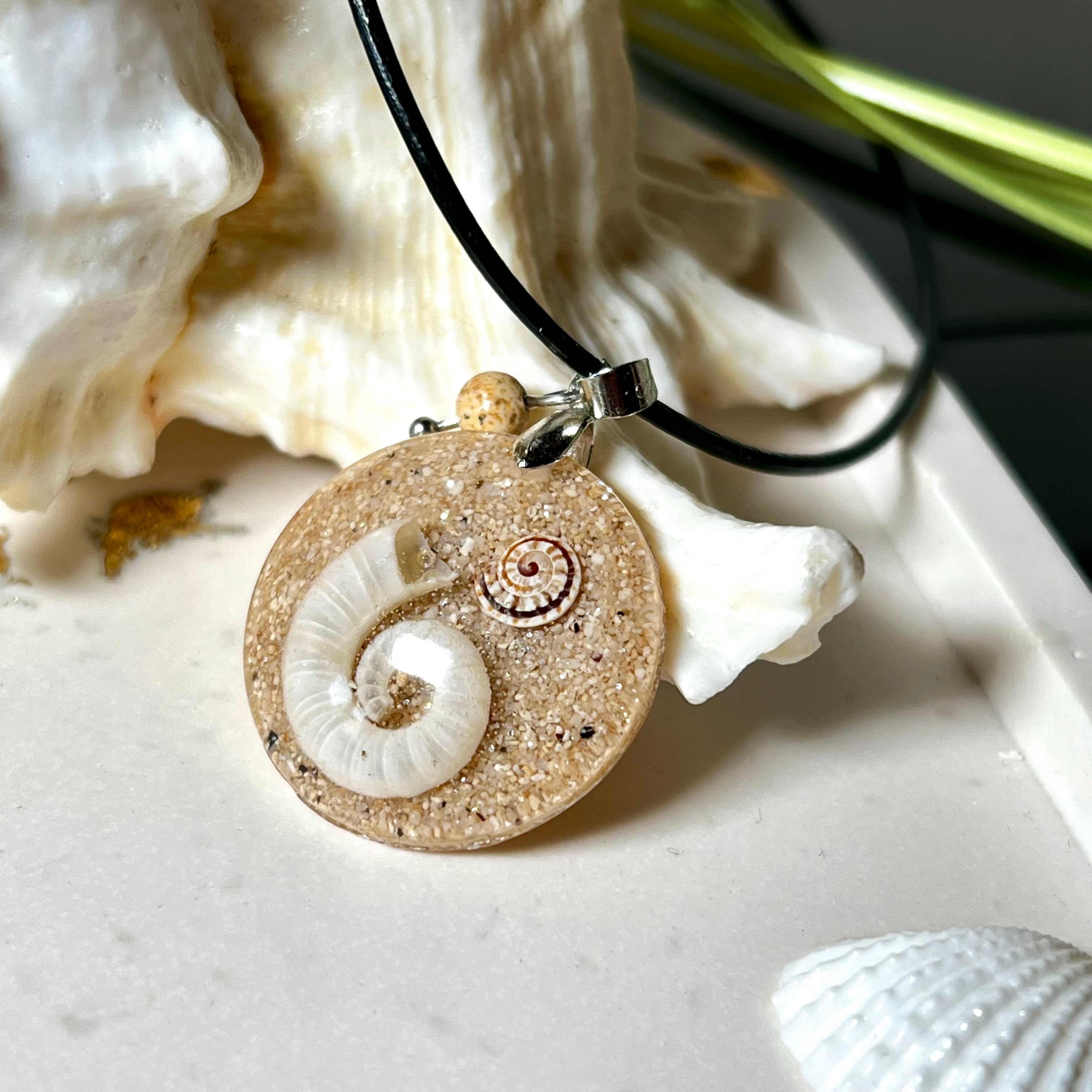 Handgemachter Anhänger mit echter Spirale, kleiner Schnecke, Meersand und feinem Glitzereffekt im Harz. Verziert mit einer Jaspisperle, Edelstahlöse und Lederkette mit Verlängerung. Maritimer Natur-Schmuck, inspiriert vom Ozean