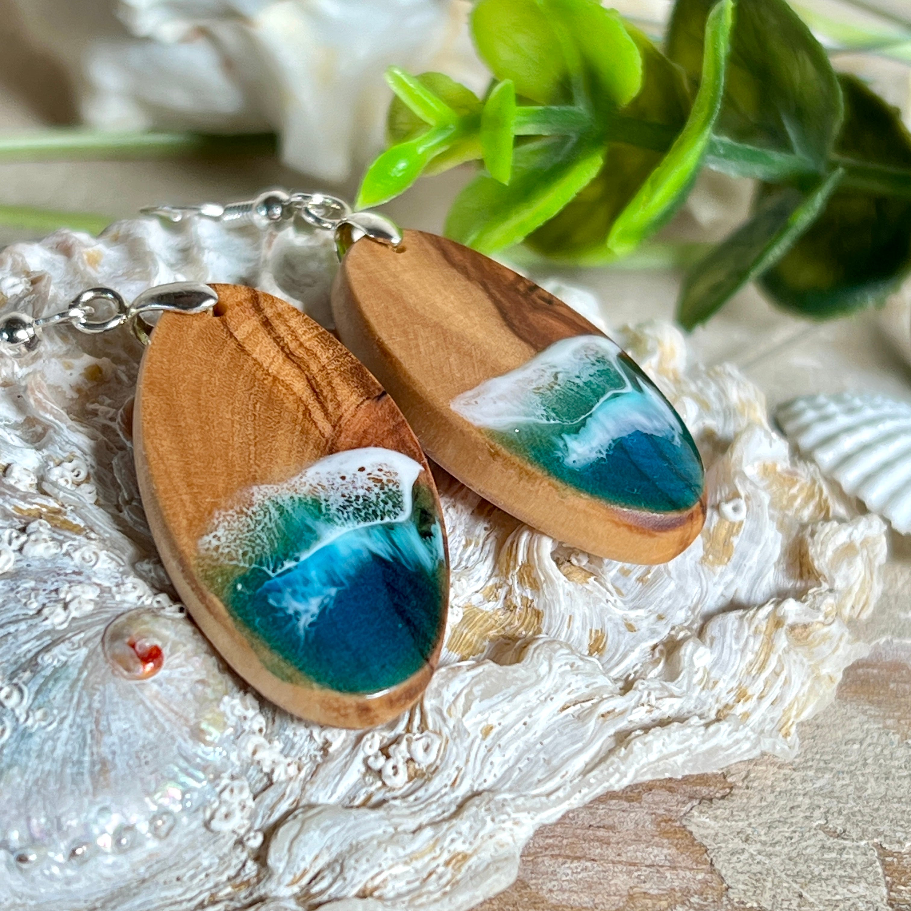 Handgefertigte Ohrringe „Wave Harmony“ aus Olivenholz und Epoxidharz in Blau-, Türkis- und Weißtönen. Das Design erinnert an Meereswellen am Strand. Jeder Ohrring ist ein Unikat mit individueller Maserung. Versilberte, nickelfreie und bleifreie Anhängerschlaufe, 925 Silber Ohrhaken. Maritimer Schmuck – perfekt für Meerliebhaber und als edles Geschenk.