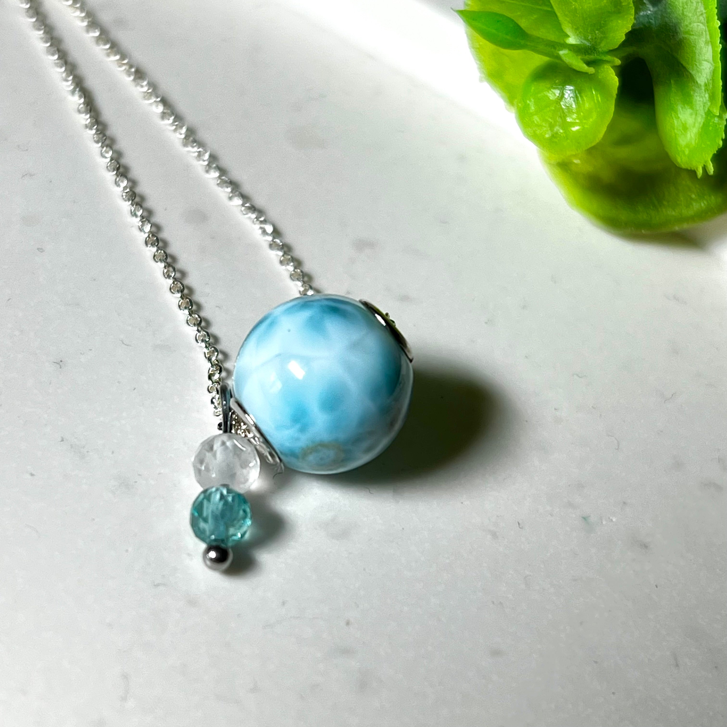 Feine Halskette aus 925er Silber mit einer polierten Larimar-Perle als Hauptstein, ergänzt durch funkelnde Apatit- und Bergkristall-Perlen. Der Edelstein mit seiner typischen Meeresfärbung erinnert an tropische Lagunen und steht für innere Ruhe und Klarheit.Ideal als Geschenk zum Geburtstag, für Meerliebhaber oder spirituelle Schmuckträgerinnen.