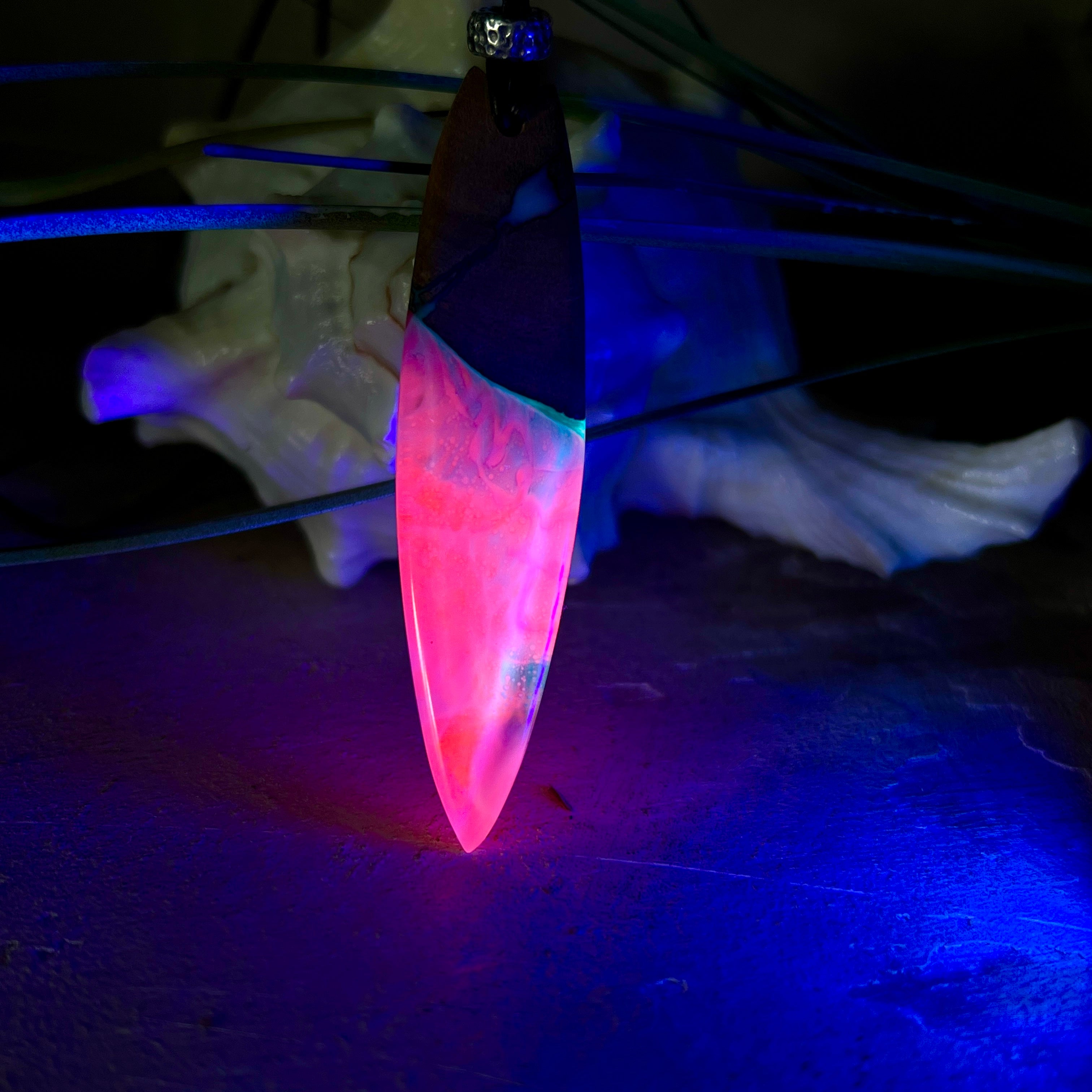 Handgefertigter Surfbrett-Anhänger aus Nussbaumholz und fluoreszierendem Epoxidharz in Pink, Blau und Weiß. Der Anhänger leuchtet zart bei Schwarzlicht und wird an einem verstellbaren Lederband (25–44 cm) mit Holzperlen getragen. Ein maritimes Unikat – ideal für Surfer und Naturliebhaber.