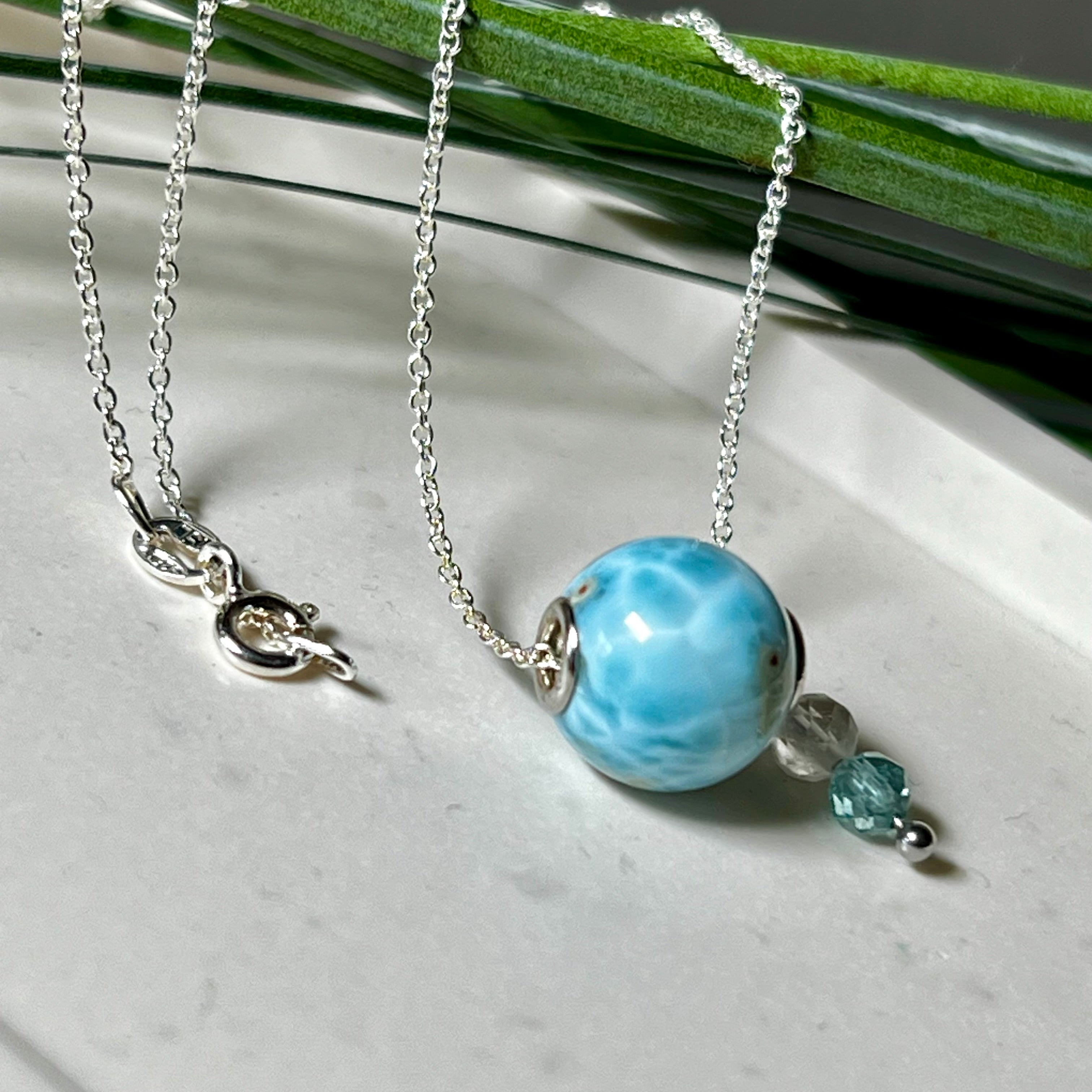 Feine Halskette aus 925er Silber mit einer polierten Larimar-Perle als Hauptstein, ergänzt durch funkelnde Apatit- und Bergkristall-Perlen. Der Edelstein mit seiner typischen Meeresfärbung erinnert an tropische Lagunen und steht für innere Ruhe und Klarheit.Ideal als Geschenk zum Geburtstag, für Meerliebhaber oder spirituelle Schmuckträgerinnen.