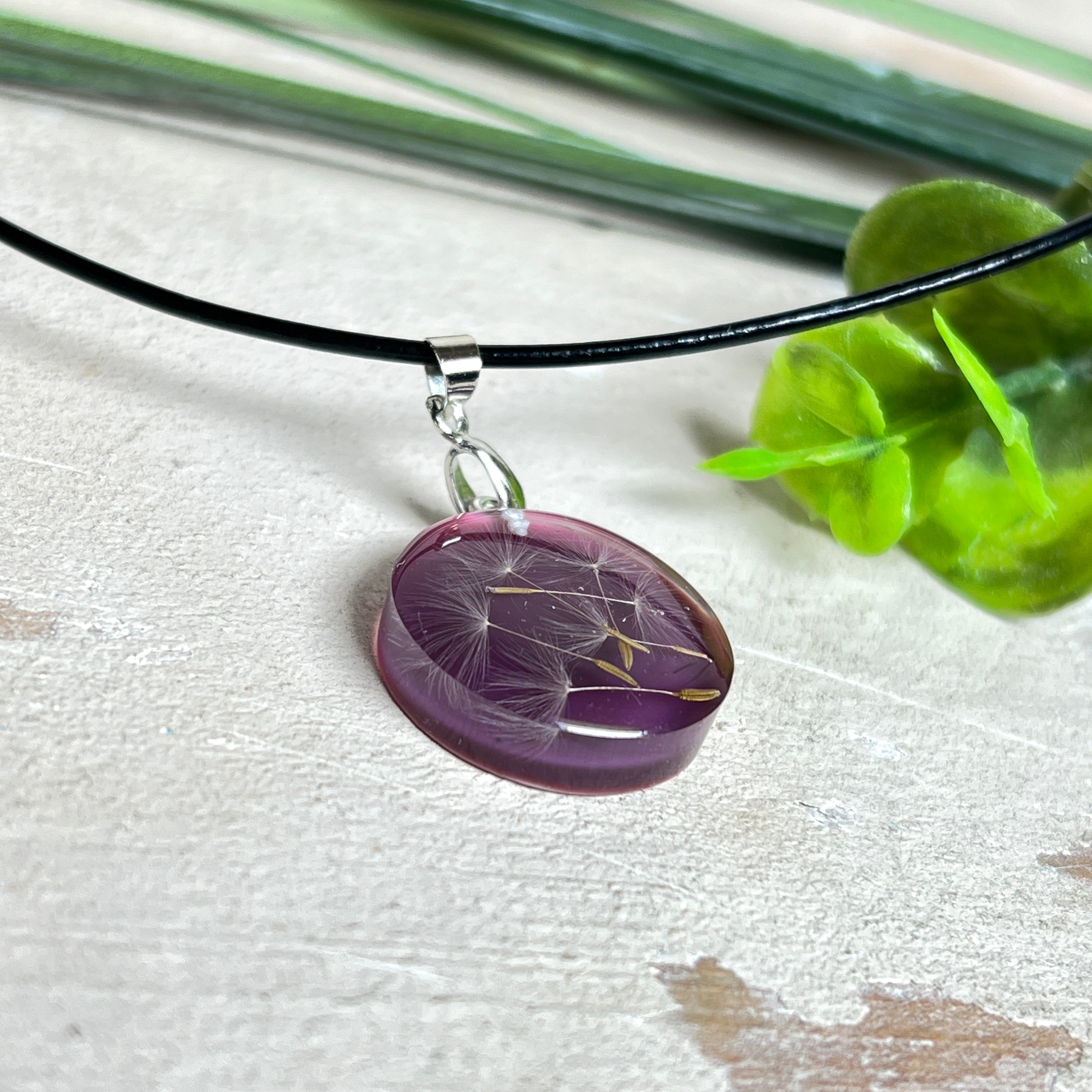 Runder Pusteblumen-Anhänger aus Harz, Hintergrund Brombeerfarben. Durchmesser 22 mm, Edelstahlöse, Lederkette verstellbar mit Edelstahlverschluss.