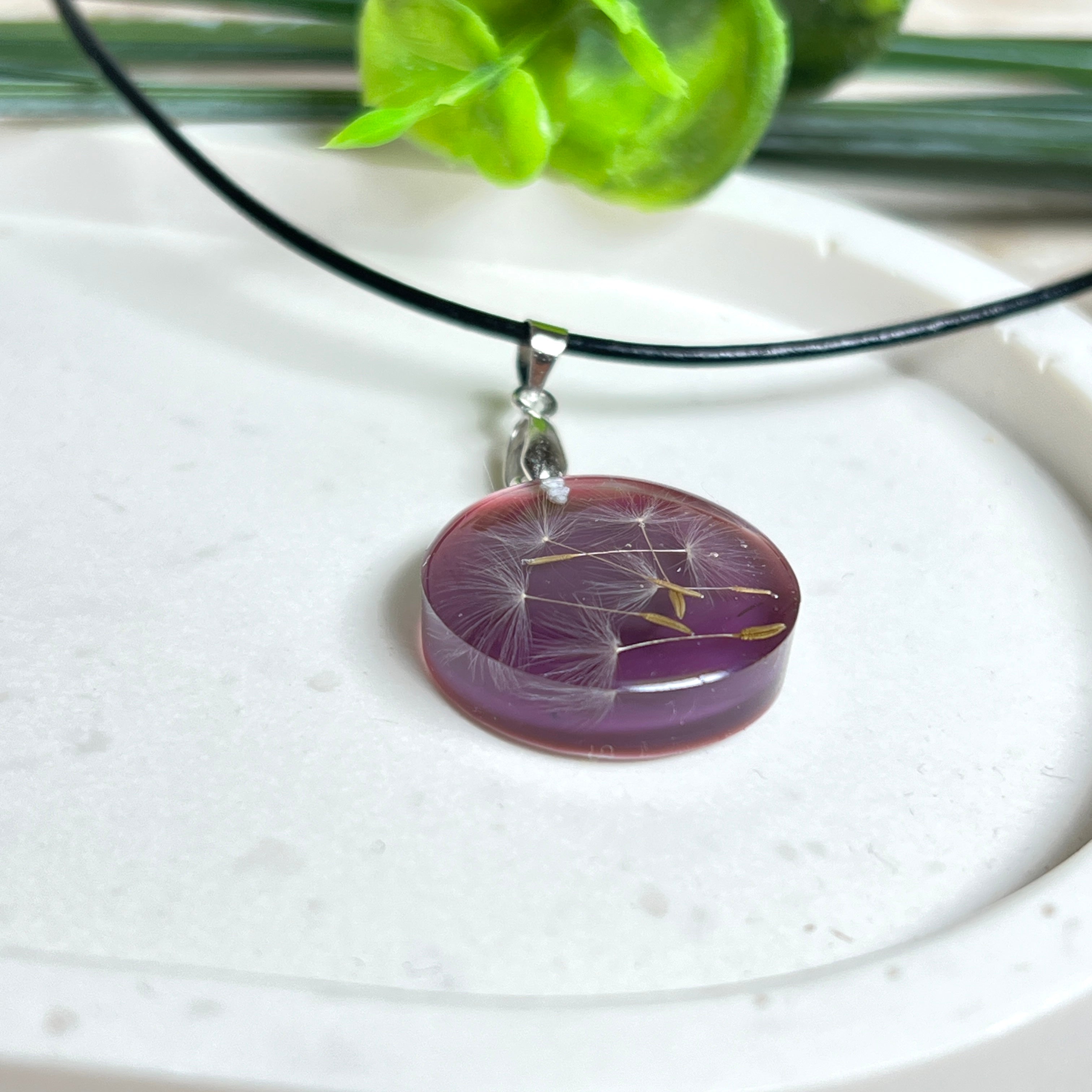 Runder Pusteblumen-Anhänger aus Harz, Hintergrund Brombeerfarben. Durchmesser 22 mm, Edelstahlöse, Lederkette verstellbar mit Edelstahlverschluss.