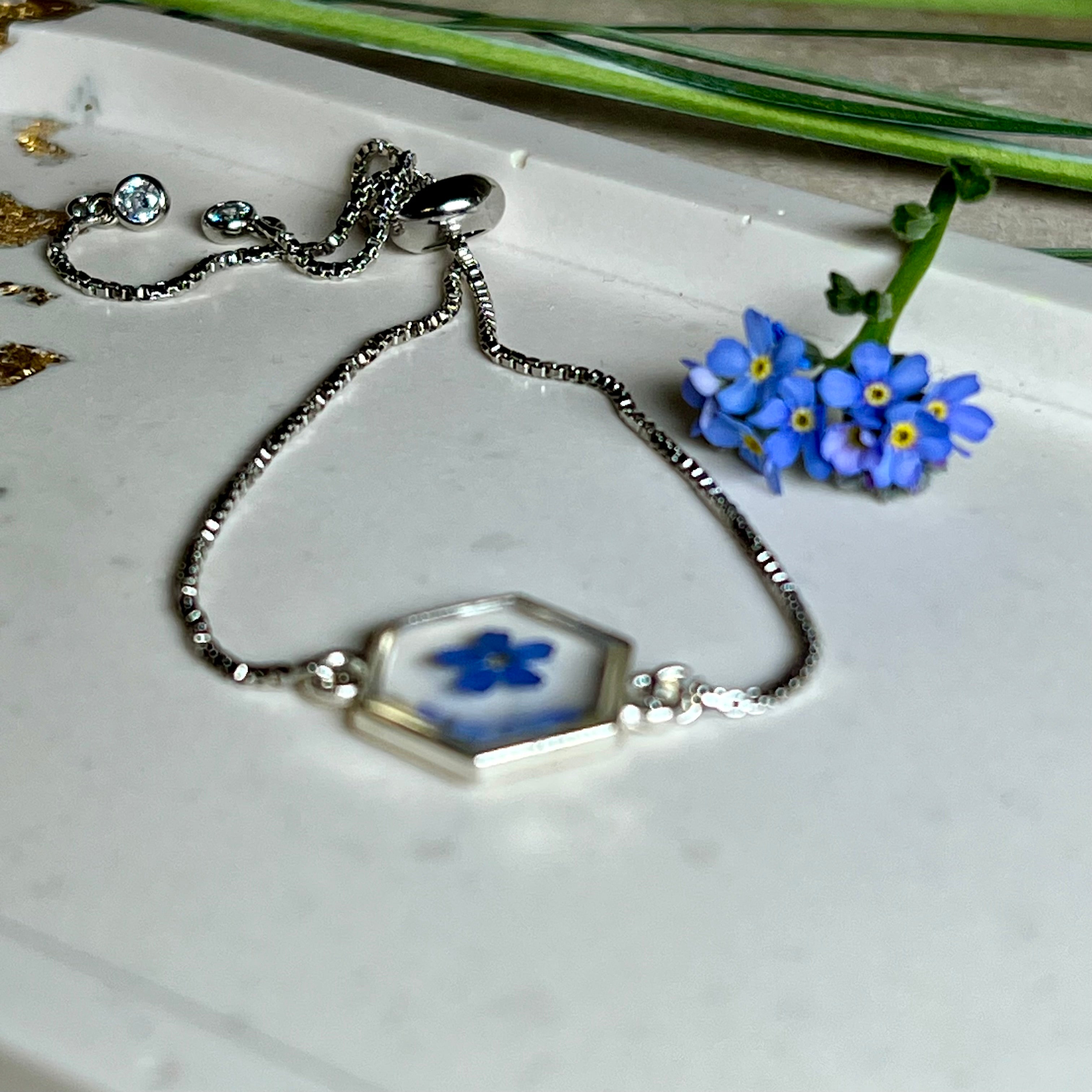„Handgefertigtes Armband mit echter Vergissmeinnicht-Blume, eingebettet in klares Harz. Verstellbares Edelstahlarmband mit Schiebeverschluss und funkelnden Zirkonia-Endperlen. Symbolträchtiger Schmuck für Frauen – ideal als Geschenk zum Muttertag, Geburtstag oder zur Erinnerung an einen besonderen Menschen.“