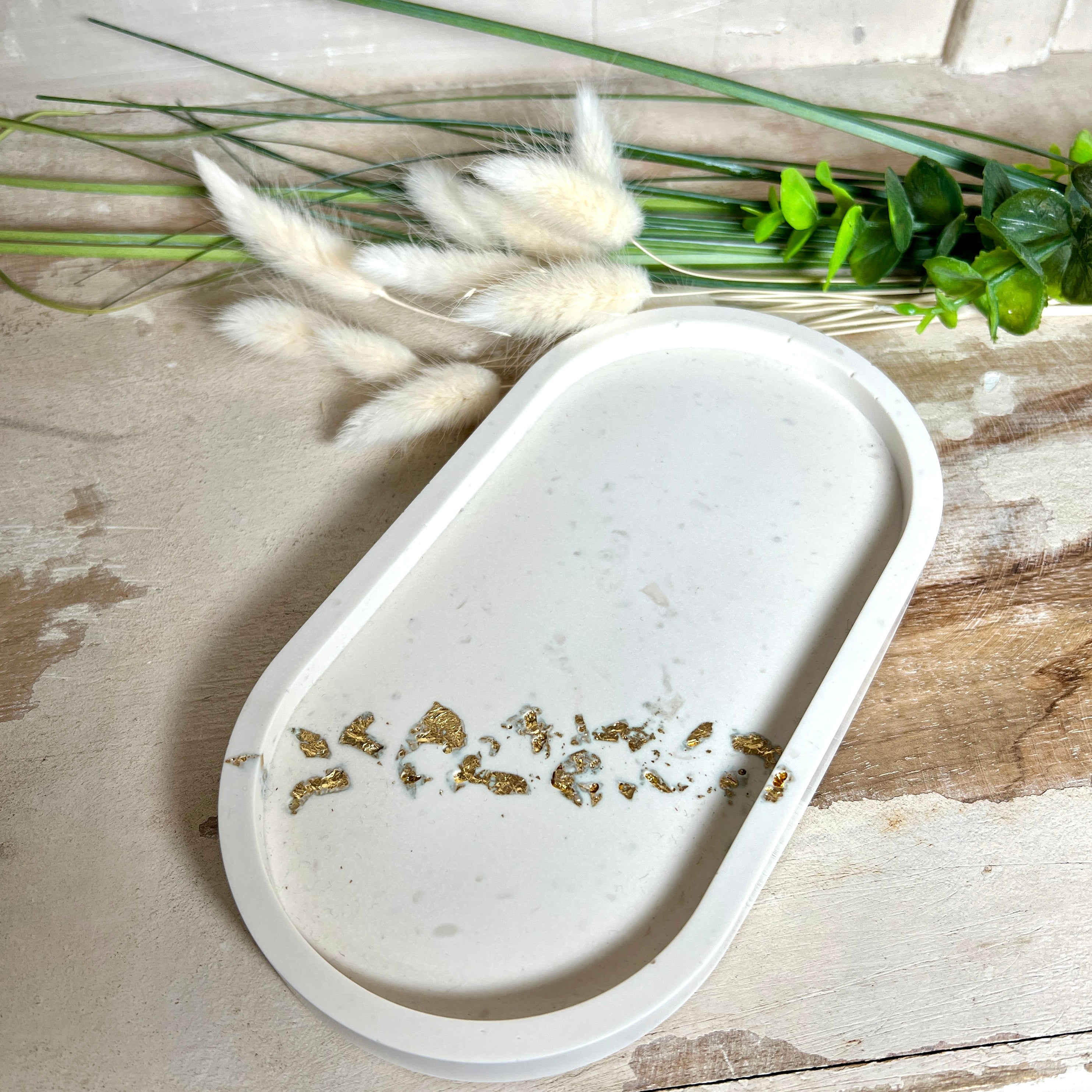 Handgefertigtes ovales Schmucktablett aus Jesmonite mit schimmernden Blattgold-Akzenten. Die Rückseite ist mit rutschfesten Korkpunkten ausgestattet. Ideal zur stilvollen Aufbewahrung von Schmuck, Schlüsseln oder kleinen Accessoires auf Kommoden und Nachttischen. Helles Design mit natürlicher Oberfläche und modernem Look. Unikat in feiner Handarbeit gefertigt – ohne Deko geliefert.