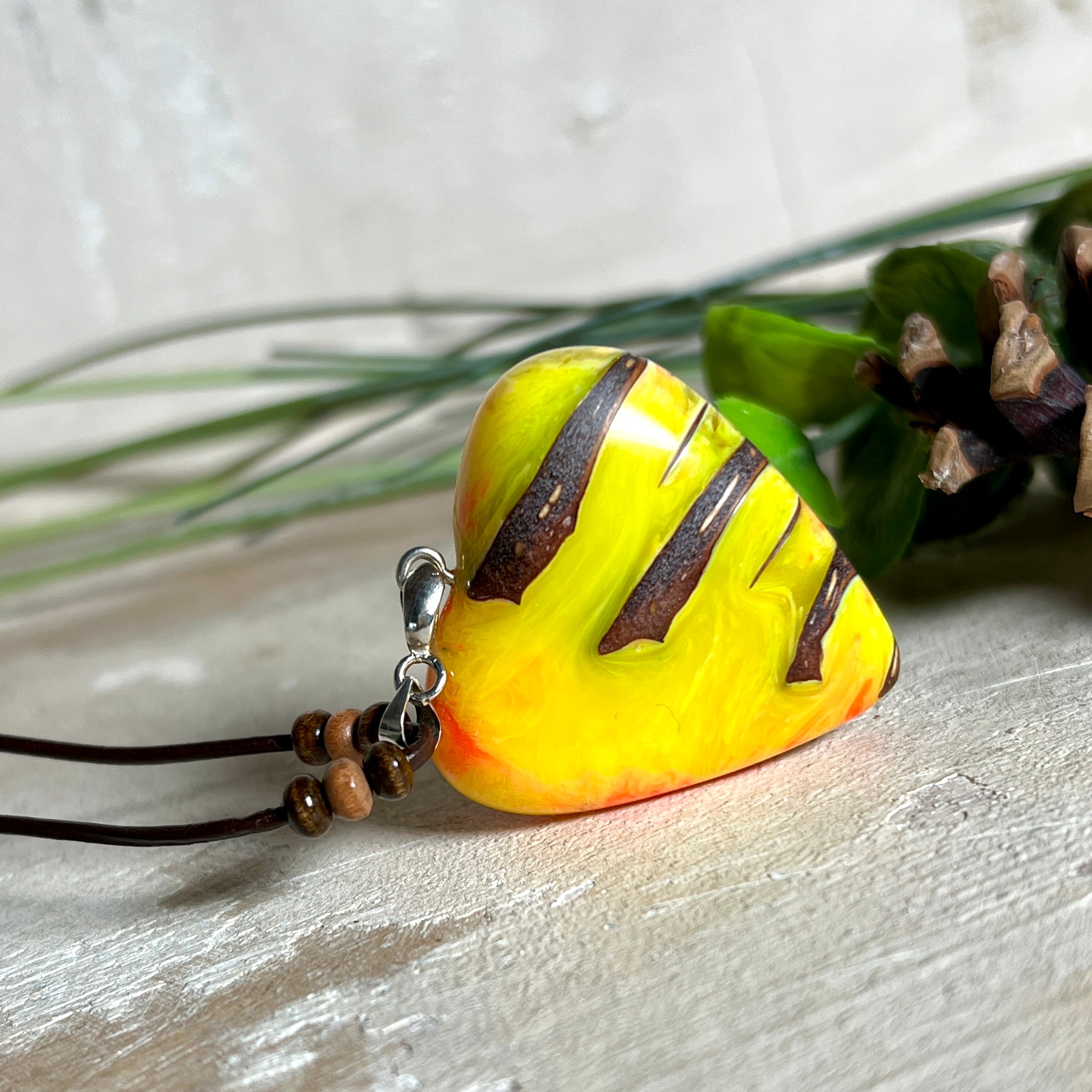 Herz-Anhänger aus Pinienzapfen & Harz, fluoreszierend bei Schwarzlicht. Farben Gelb-Orange-Weiß, Größe 4,2 × 3,8 cm. Lederband verstellbar.