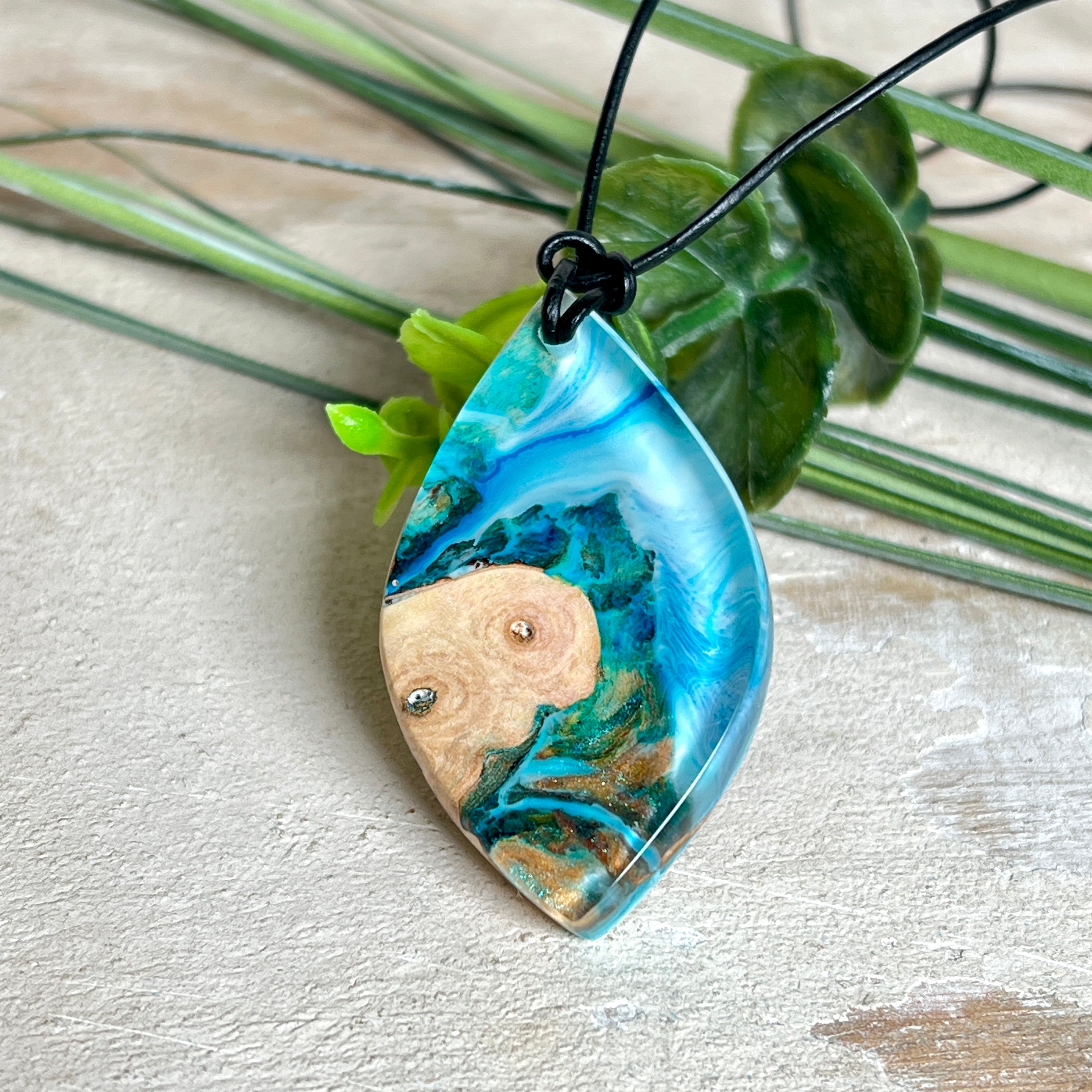 Handgefertigter Anhänger „Ocean Leaf“ aus Maserholz und Epoxidharz in Blau- und Türkistönen. Ein einzigartiges Schmuckstück, das die Schönheit von Natur und Meer einfängt. Mit verstellbarem Lederband (24–43 cm). Jeder Anhänger ist ein Unikat mit einzigartiger Maserung und Farbverlauf.