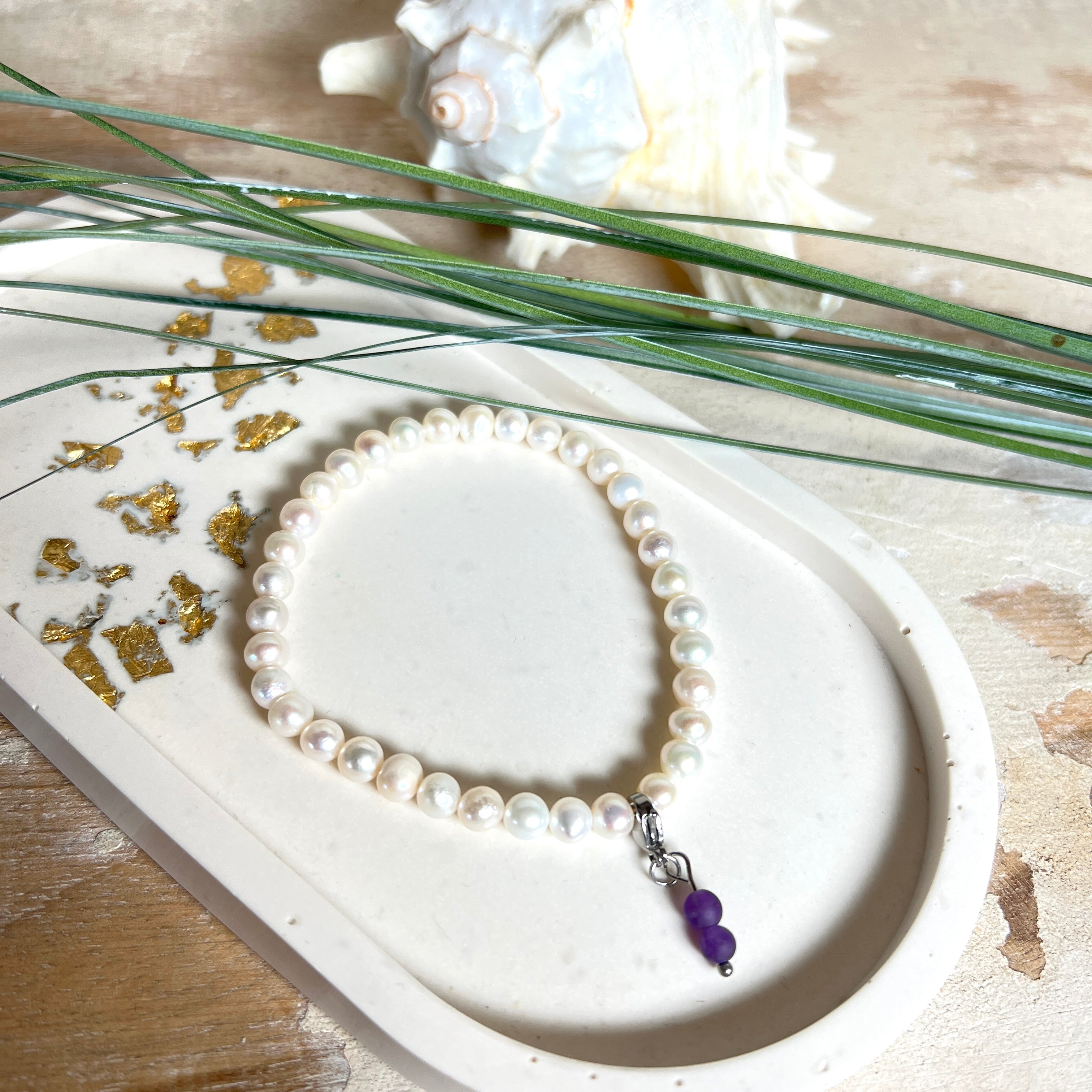 Handgefertigtes Armband „Sea Harmony“ mit schimmernden Süßwasserperlen (Ø ca. 6–7 mm), jede Perle ein Unikat. Auf elastischem Band gefädelt, mit einem filigranen Charmanhänger aus Amethyst-Perlen, befestigt an einem robusten Edelstahl-Karabiner. Ein Schmuckstück voller Eleganz, maritimer Harmonie und symbolischer Tiefe – ideal als Geschenk oder als stilvolles Accessoire.