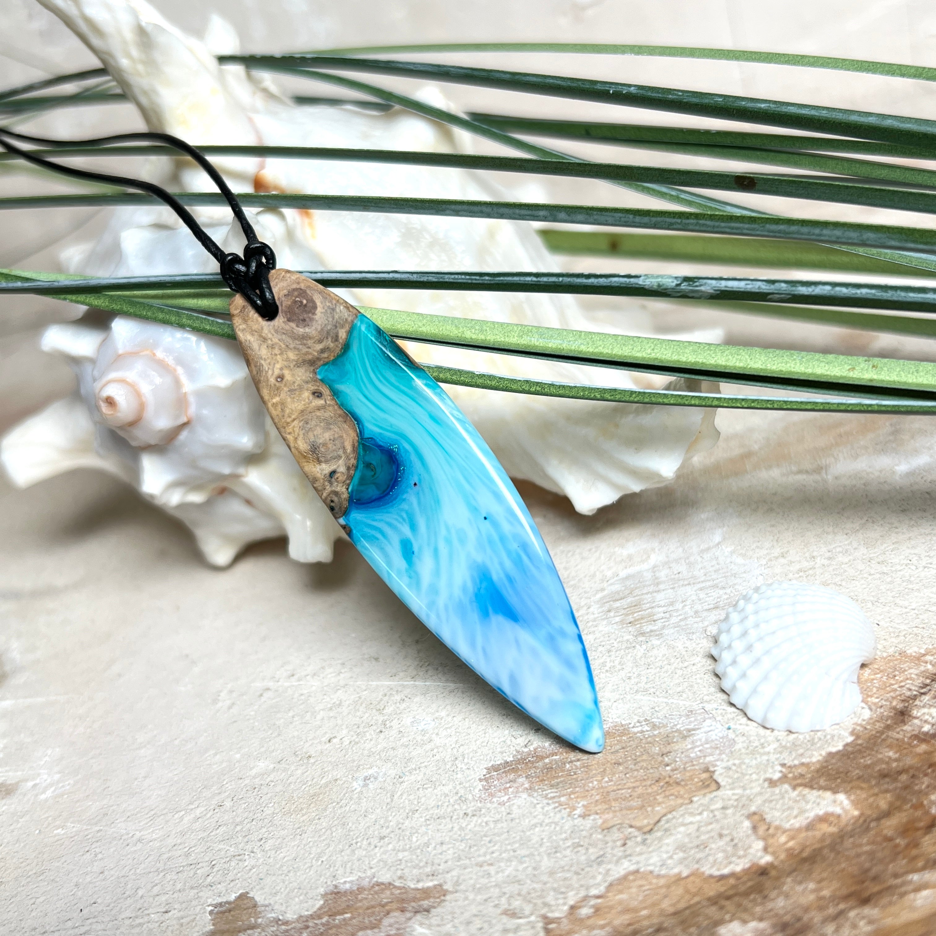 Surfbrett-Anhänger handgefertigt aus Maserholz & Harz in Blau-Weiß. Größe ca. 6,3 × 2 cm. Lederband verstellbar 26–47 cm, Schiebeknoten mit Holzperlen.