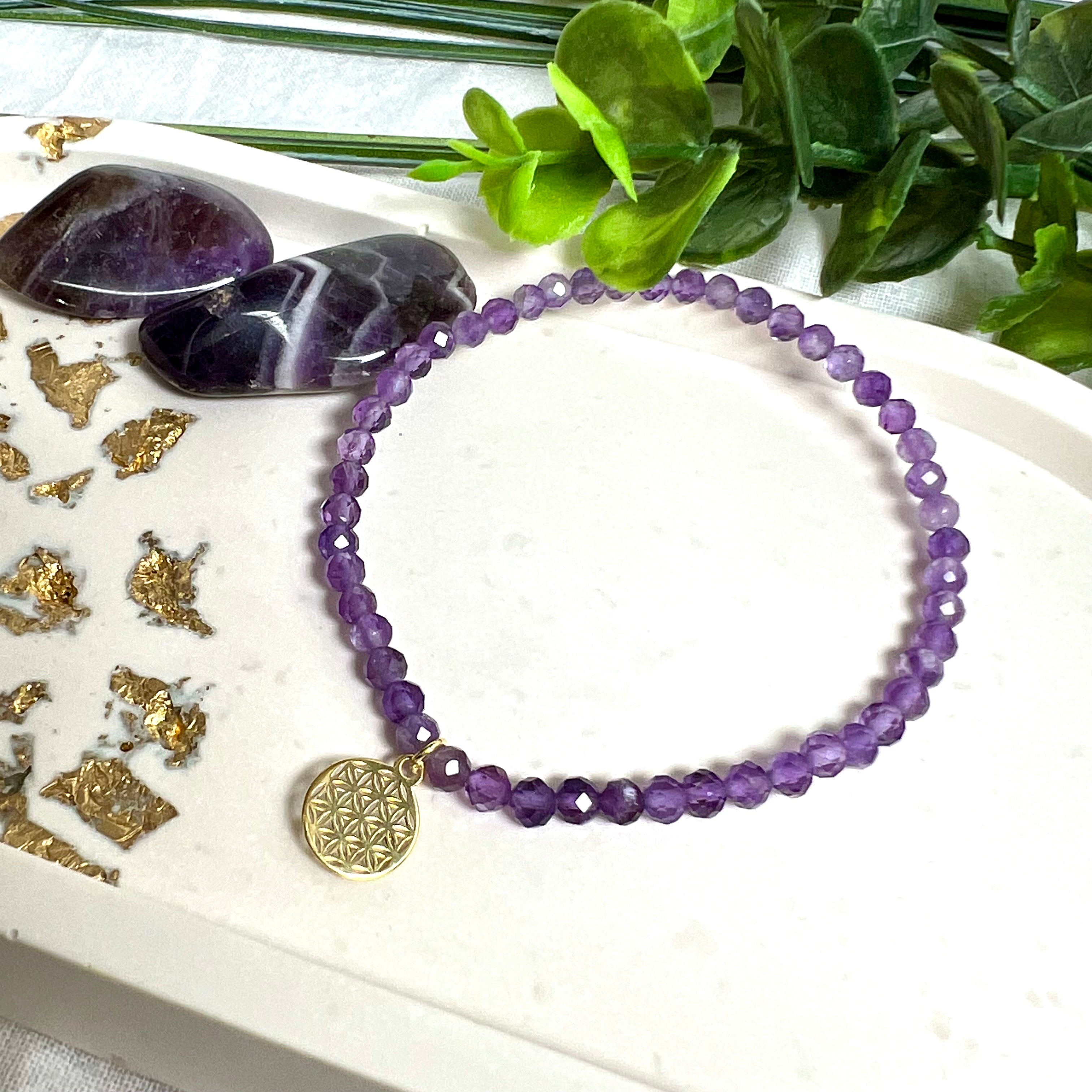 Handgefertigtes Amethyst-Armband mit facettierten 4 mm Edelstein-Perlen in zartem Violett, ergänzt durch einen vergoldeten 925 Silber Charm in Form der Blume des Lebens. Elastisches Design mit ca. 17 cm Innendurchmesser. Elegant, spirituell und fein – ein besonderes Schmuckstück für Achtsamkeit, Energie und Harmonie im Alltag.