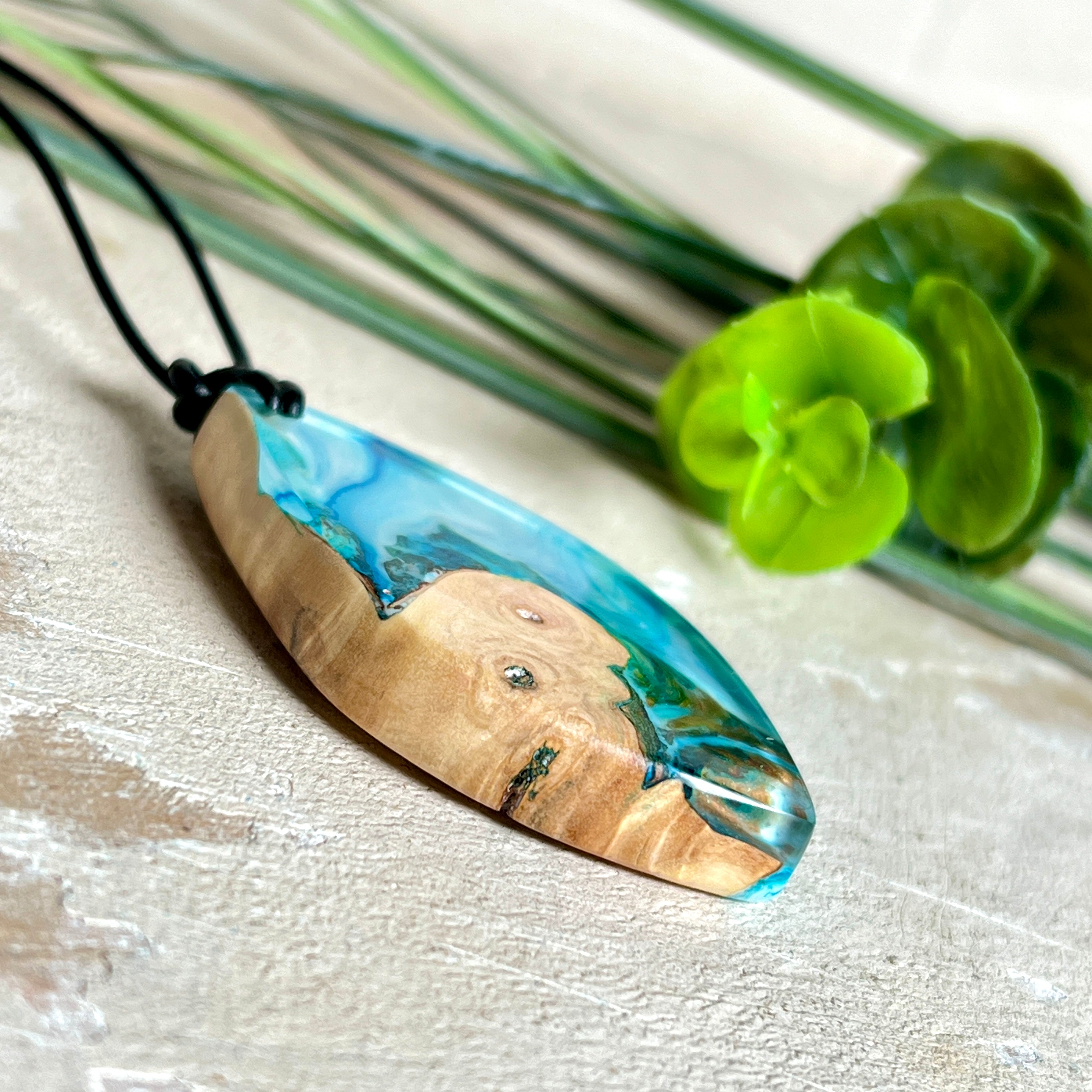 Handgefertigter Anhänger „Ocean Leaf“ aus Maserholz und Epoxidharz in Blau- und Türkistönen. Ein einzigartiges Schmuckstück, das die Schönheit von Natur und Meer einfängt. Mit verstellbarem Lederband (24–43 cm). Jeder Anhänger ist ein Unikat mit einzigartiger Maserung und Farbverlauf.
