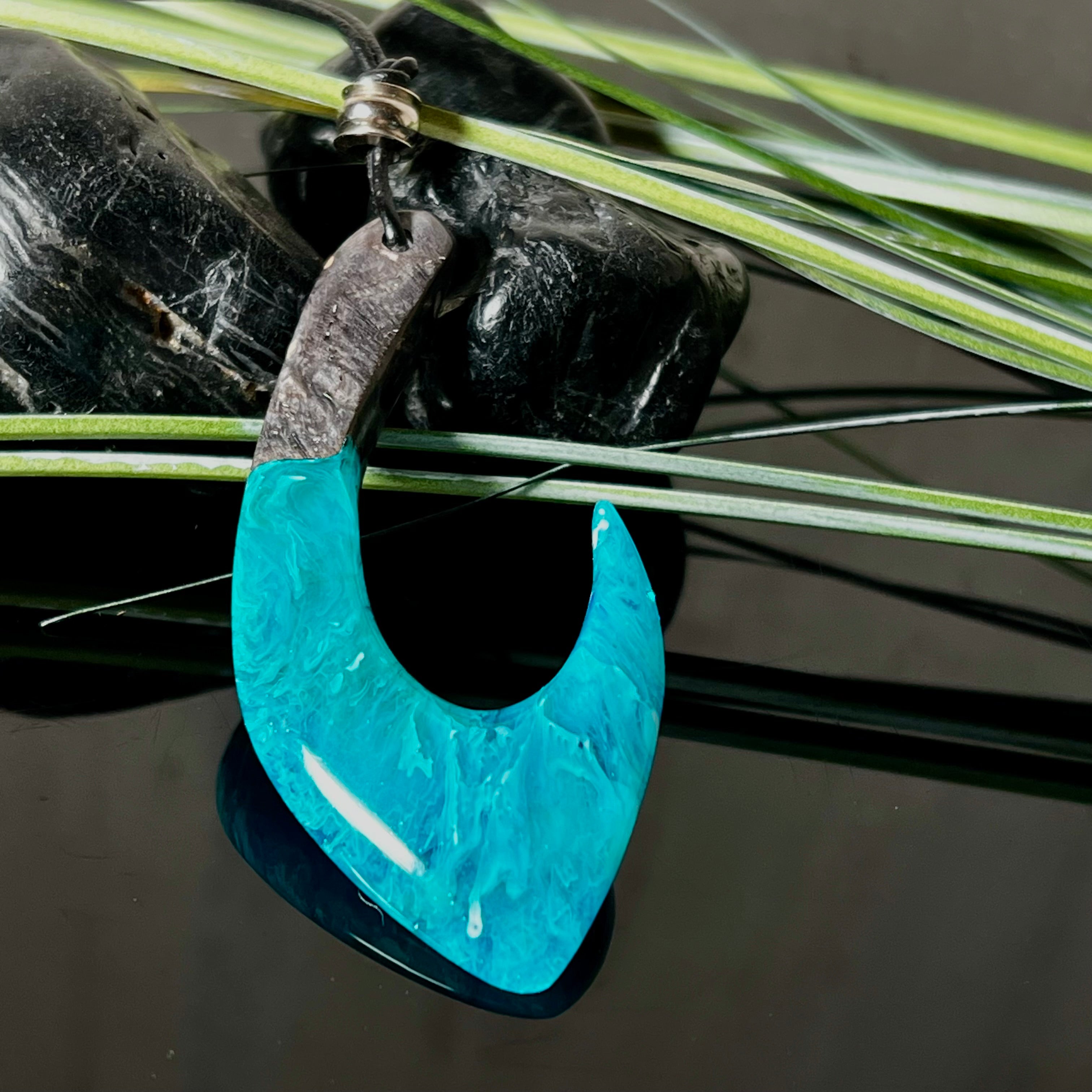 Handgefertigter Maori-Anhänger „Tangaroa Spirit“ in traditioneller Hakenform, gefertigt aus stabilisiertem Maserholz und ozeanblauem Harz. Die polierte Oberfläche bringt die natürlichen Maserungen und das tiefblaue Farbspiel besonders zur Geltung. Symbolisiert Schutz, Stärke und die Verbundenheit zum Meer. Verstellbares Lederband mit Schiebeknoten und dekorativen Holz- sowie Metallperlen – ideal als kraftvoller Talisman oder Geschenk.