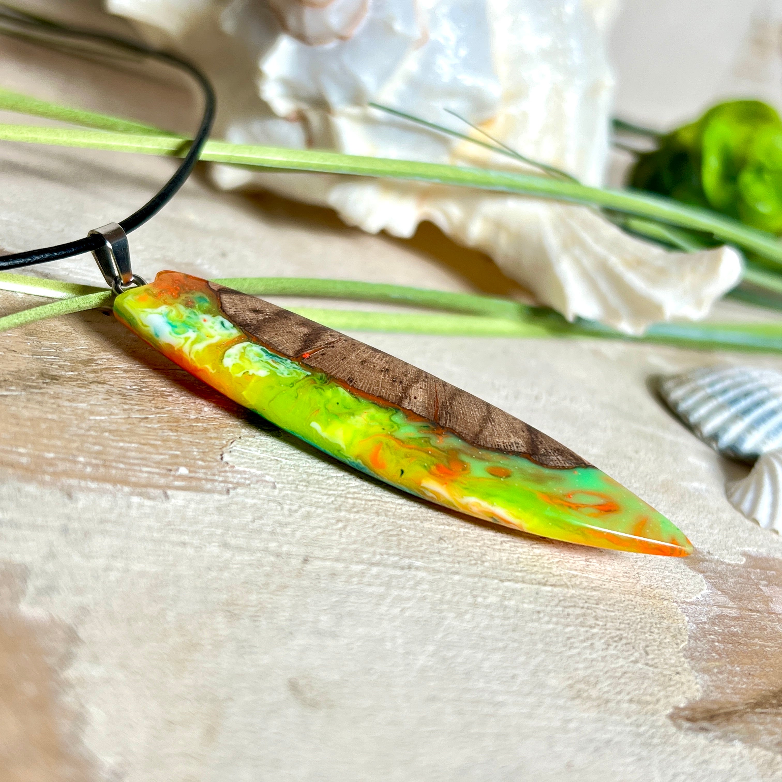Handgefertigte Halskette „Tropical Glow“ mit Surfbrett-Anhänger aus naturbelassenem Rebholz (Weinrebe) und marmoriertem Epoxidharz in Grün, Orange, Türkis und Weiß. Größe des Anhängers ca. 6,5 × 2 cm. Das Harz fluoresziert eindrucksvoll unter UV-/Schwarzlicht. Edelstahl-Anhängerschlaufe, schwarze Lederkette (45 cm + 5 cm Verlängerung) mit Edelstahl-Karabiner. Unikat in maritim-sommerlichem Stil, ideal als besonderes Geschenk.