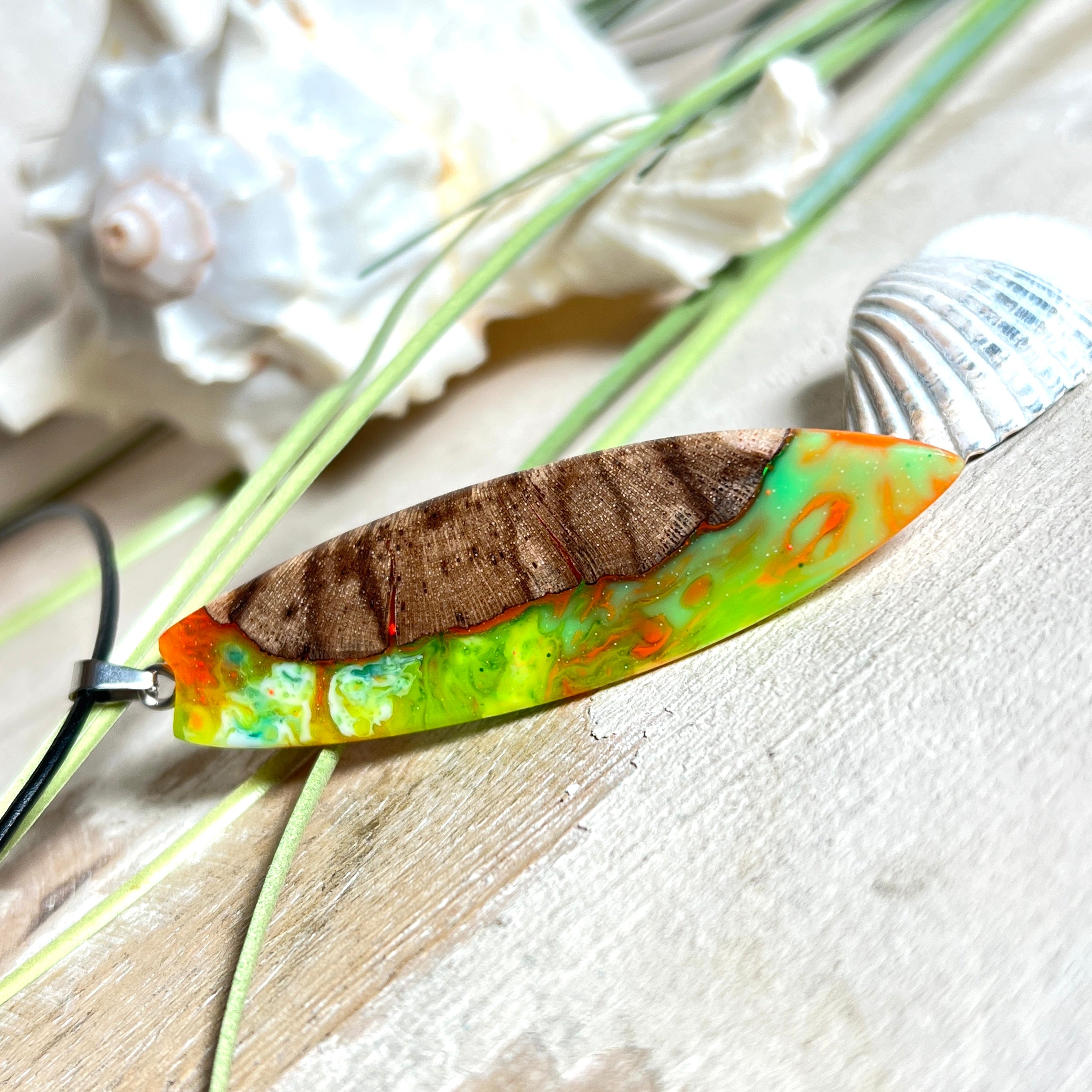 Handgefertigte Halskette „Tropical Glow“ mit Surfbrett-Anhänger aus naturbelassenem Rebholz (Weinrebe) und marmoriertem Epoxidharz in Grün, Orange, Türkis und Weiß. Größe des Anhängers ca. 6,5 × 2 cm. Das Harz fluoresziert eindrucksvoll unter UV-/Schwarzlicht. Edelstahl-Anhängerschlaufe, schwarze Lederkette (45 cm + 5 cm Verlängerung) mit Edelstahl-Karabiner. Unikat in maritim-sommerlichem Stil, ideal als besonderes Geschenk.