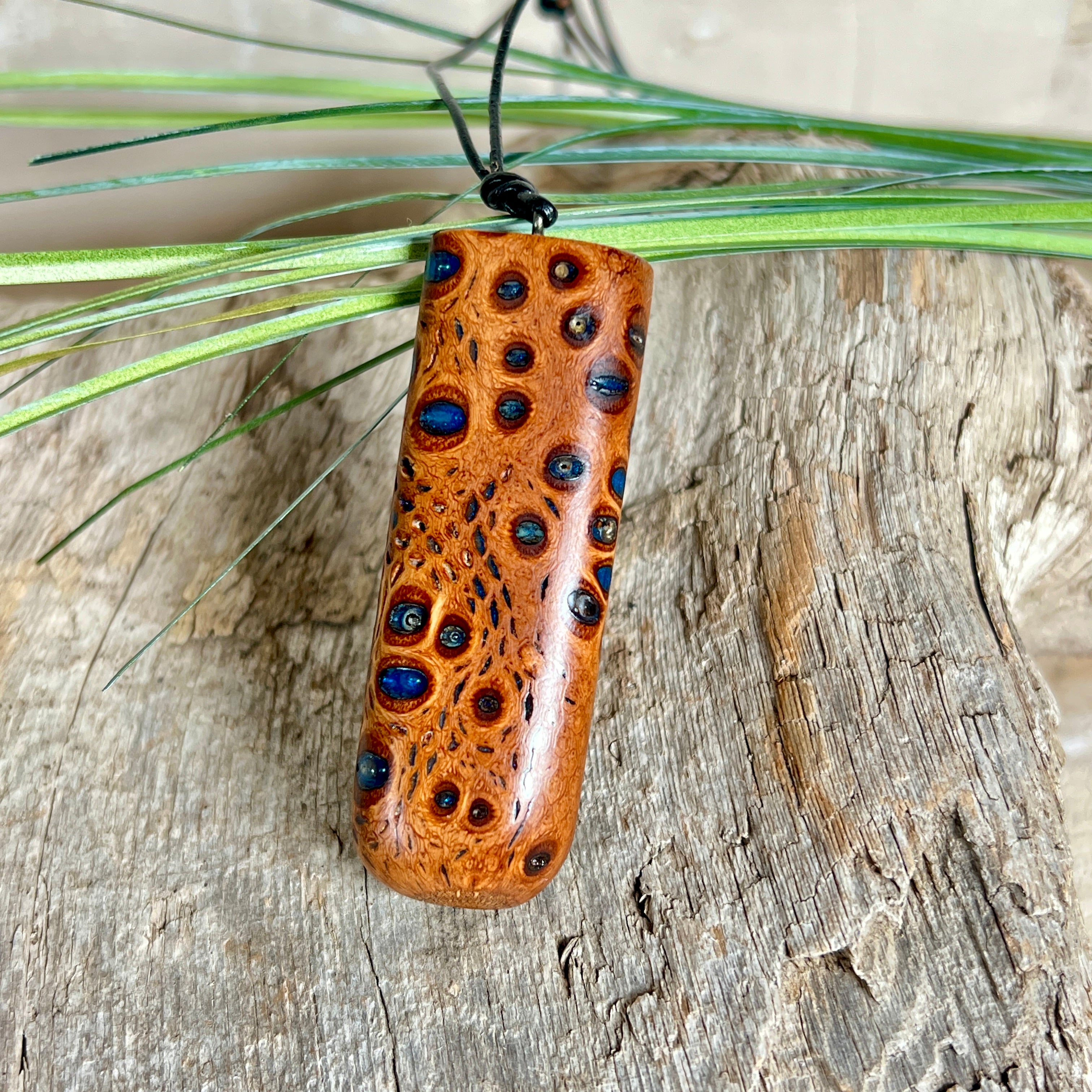 Handgefertigter Anhänger aus australischem Banksiazapfen und gegossenem Harz in Blau. Der rechteckige Anhänger (5,5 x 2 cm) zeigt eine charakteristische Maserung mit markanten Löchern, die durch die Samenstruktur des Zapfens entstehen. Das Lederband ist verstellbar (29–51 cm) und mit Holzperlen verziert. Ein edles Natur-Unikat.
