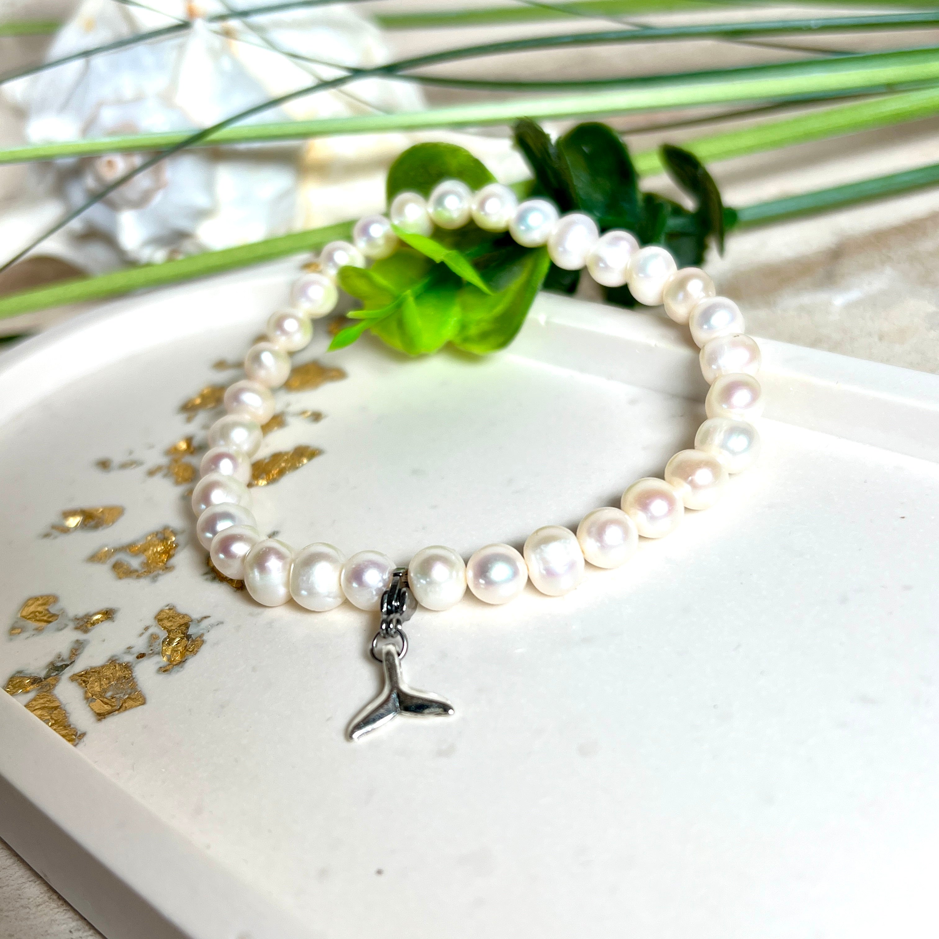 Handgefertigtes Armband aus echten Süßwasserperlen (ca. 6-7 mm), elastisch aufgezogen mit einem Edelstahl-Charm in Form einer Walflosse. Maritimes Design mit Bedeutung – stilvoll, natürlich und elegant. Größe ca. 17,5 cm. Ideal als Geschenk für Meeresliebhaberinnen oder für sich selbst.