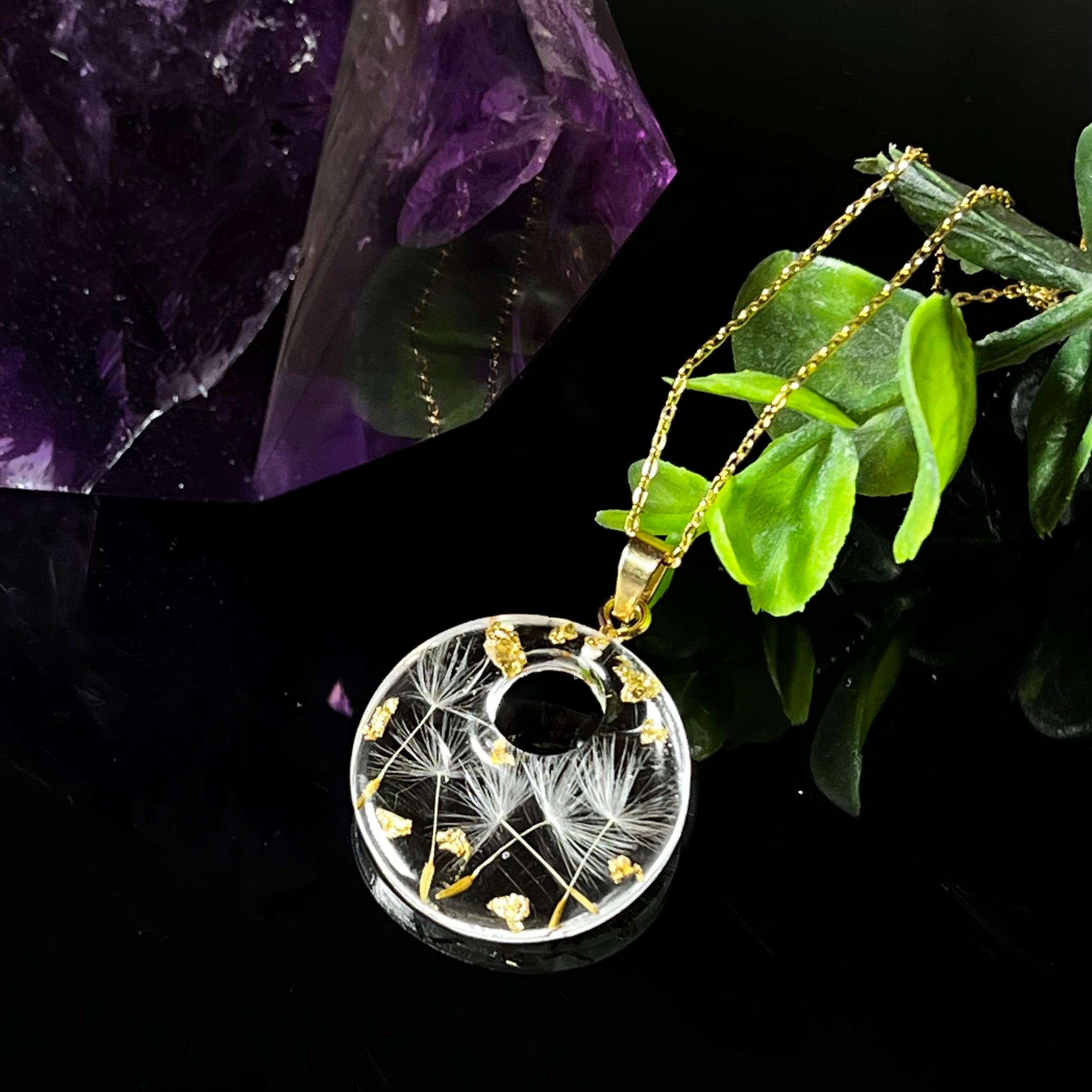 Runder Harzanhänger mit echten Pusteblumensamen und zarten Blattgold-Akzenten auf einer vergoldeten 925 Silberkette, 45 cm lang. Der Anhänger hat einen Durchmesser von ca. 2,6 cm und wird von einer goldfarbenen Edelstahlöse gehalten. Das Design symbolisiert Leichtigkeit, Hoffnung und Naturverbundenheit – perfekt als Geschenk oder für Naturliebhaberinnen. Liebevoll von Hand gefertigt und ein echtes Unikat.