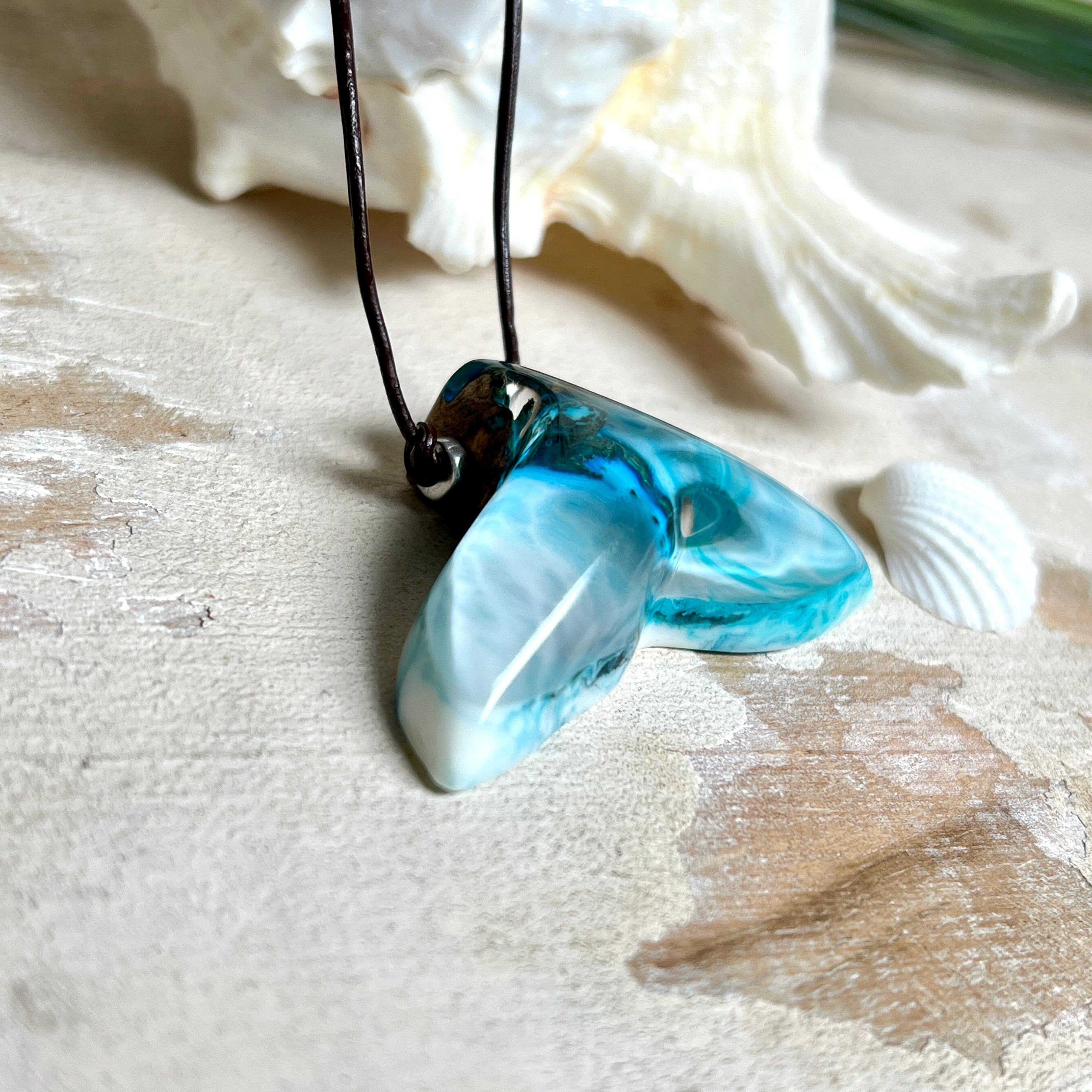 Walflossen-Anhänger „Flossenklang“ – handgefertigtes Unikat aus Maserholz und türkis-blau-grauen und weißem Harz. Die elegant geschwungene Form erinnert an die Flosse eines Wals und symbolisiert Freiheit, Stärke und Naturverbundenheit. Mit verstellbarem braunem Lederband gefertigt, ist jedes Stück ein individuelles Schmuckstück für Meeresliebhaber und Natursuchende. Maritimer Halsschmuck, inspiriert vom Ozean, glatt poliert und mit Liebe zum Detail von Hand gearbeitet.