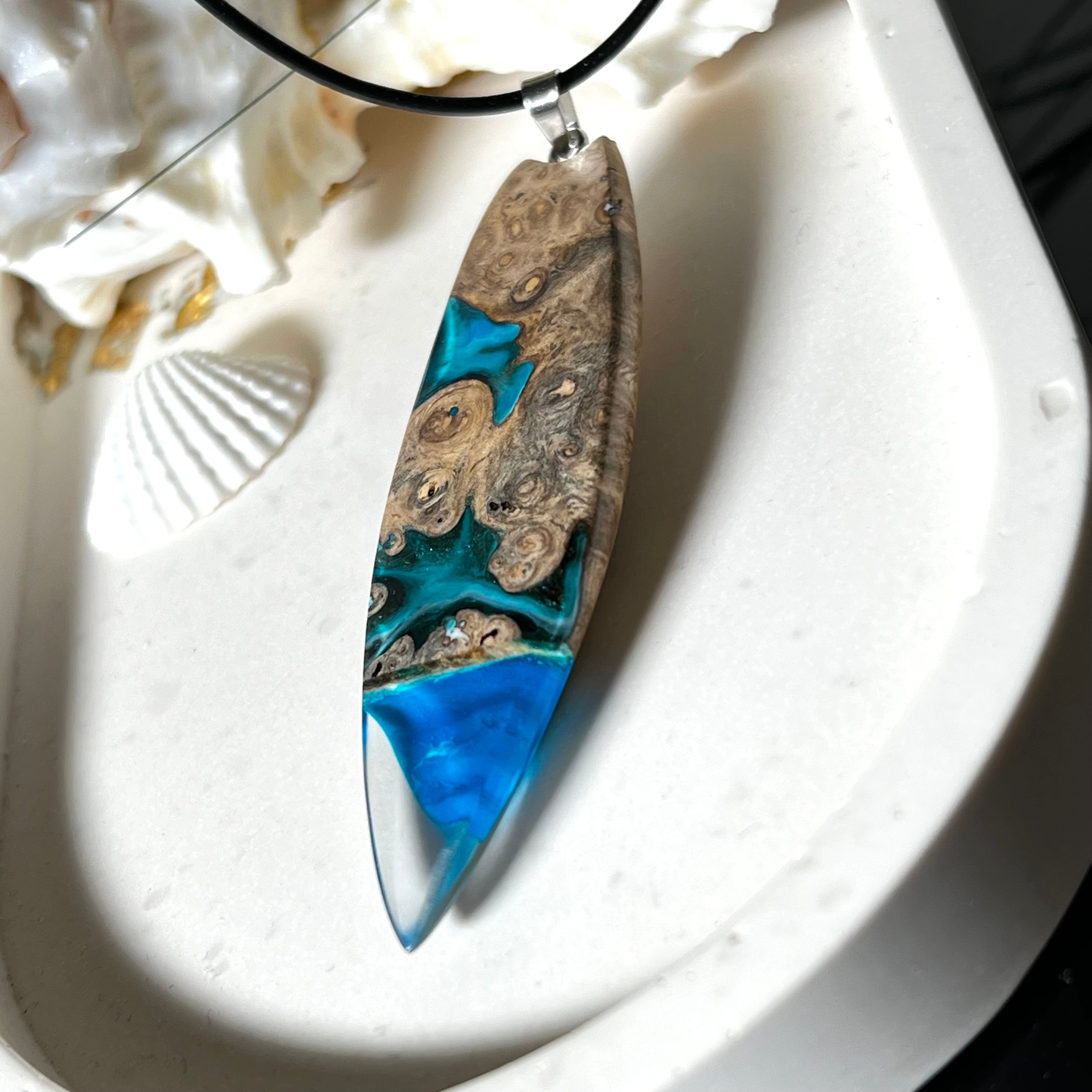 Handgefertigter Surfbrett-Anhänger aus Maserholz und transparentem Harz mit Farbverlauf in Blau und Weiß. Die natürliche Maserung des Holzes trifft auf ozeanartige Harzstrukturen. Größe ca. 6,7 x 2 cm, mit Edelstahlöse und Lederband inkl. Karabinerverschluss (45 cm + 5 cm Verlängerung). Jedes Stück ist ein Unikat – maritim, modern und mit viel Liebe gefertigt.