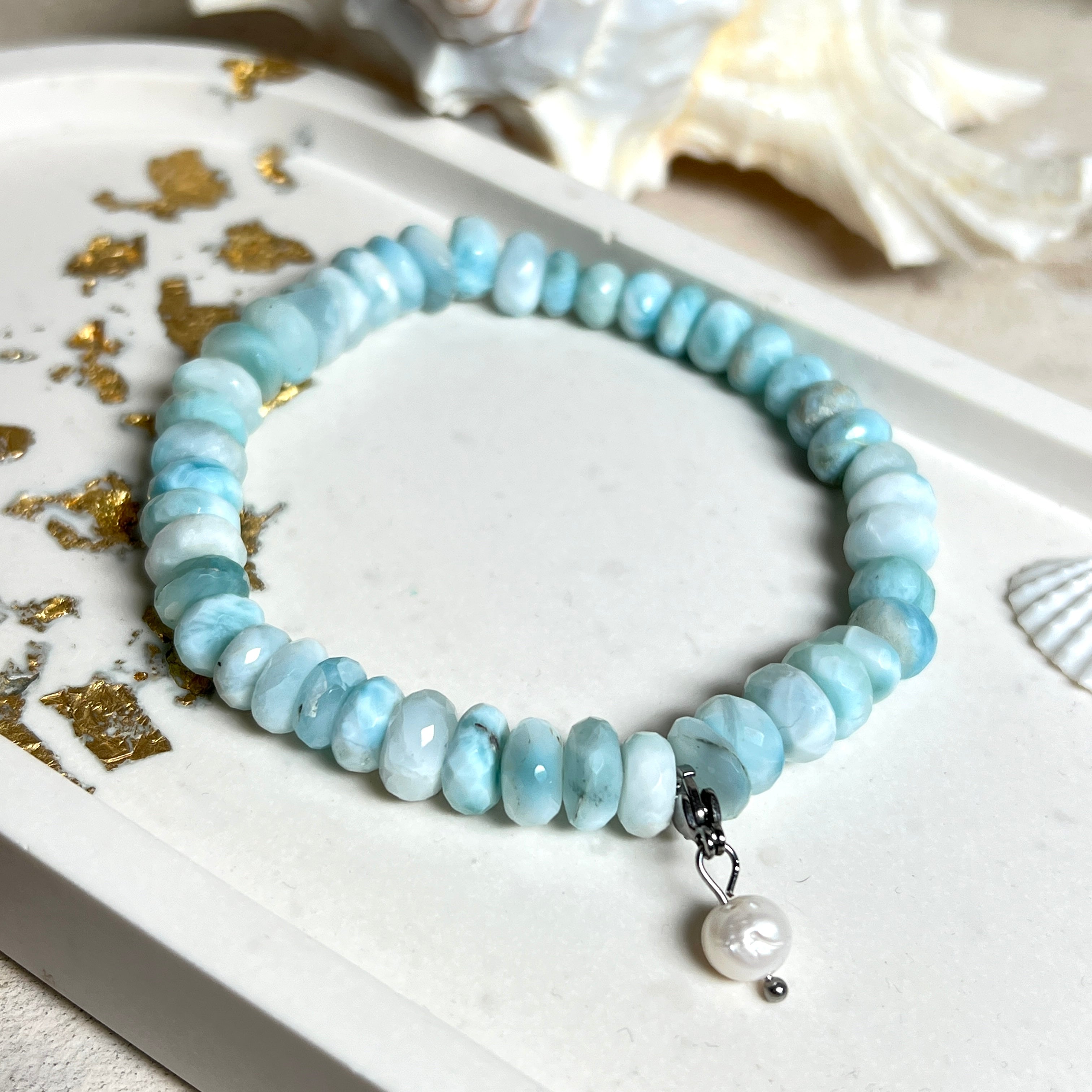 Handgefertigtes Armband aus seltenem Larimar mit facettierten, türkis-blauen Edelsteinperlen (Ø ca. 6–7 mm), elastischem Band und einem zarten Süßwasserperlen-Charm an Edelstahlkarabiner. Der wertvolle Larimar, auch „Stein des Atlantis“ genannt, gilt als Edelstein der Ruhe und Meeresverbundenheit.