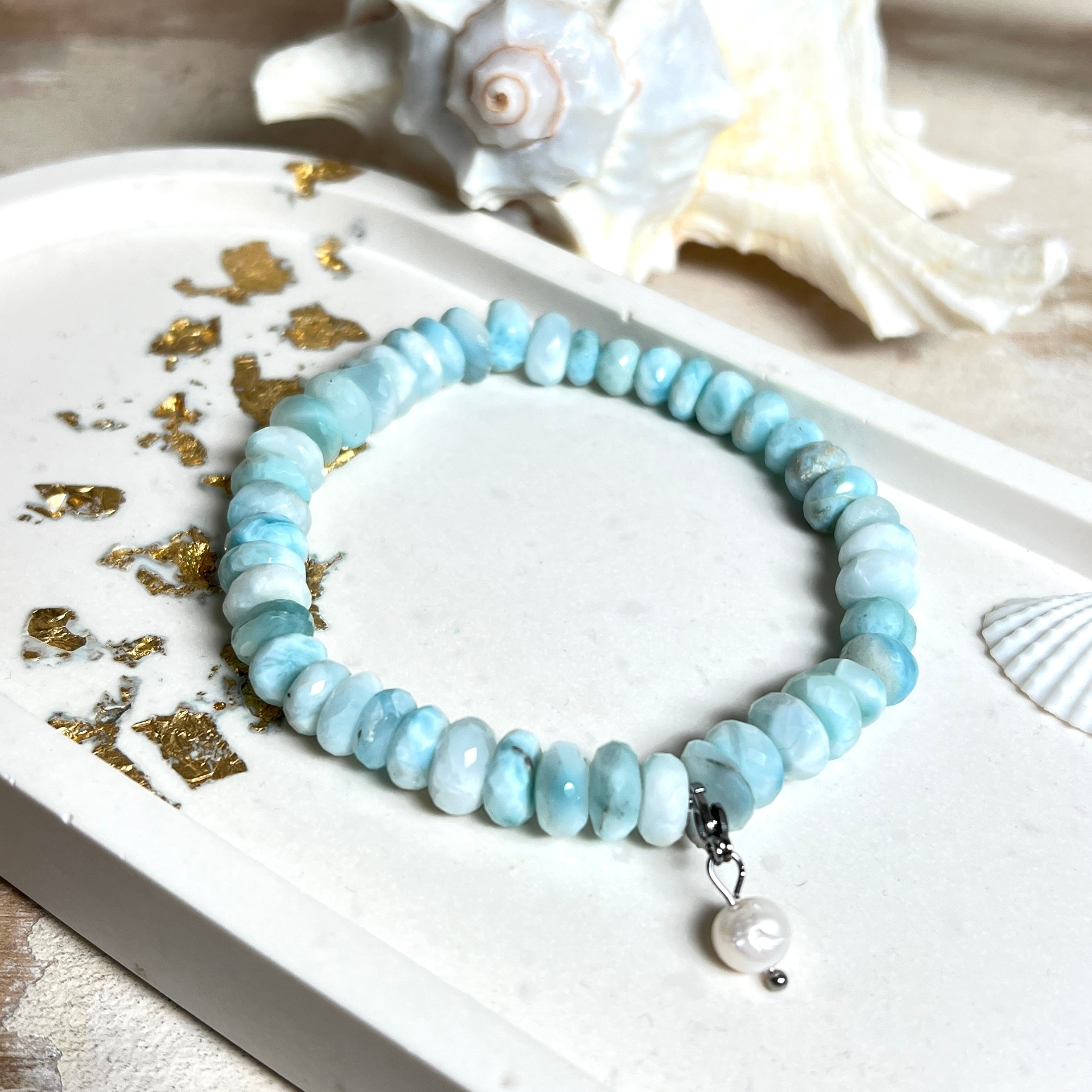 Handgefertigtes Armband aus seltenem Larimar mit facettierten, türkis-blauen Edelsteinperlen (Ø ca. 6–7 mm), elastischem Band und einem zarten Süßwasserperlen-Charm an Edelstahlkarabiner. Der wertvolle Larimar, auch „Stein des Atlantis“ genannt, gilt als Edelstein der Ruhe und Meeresverbundenheit.