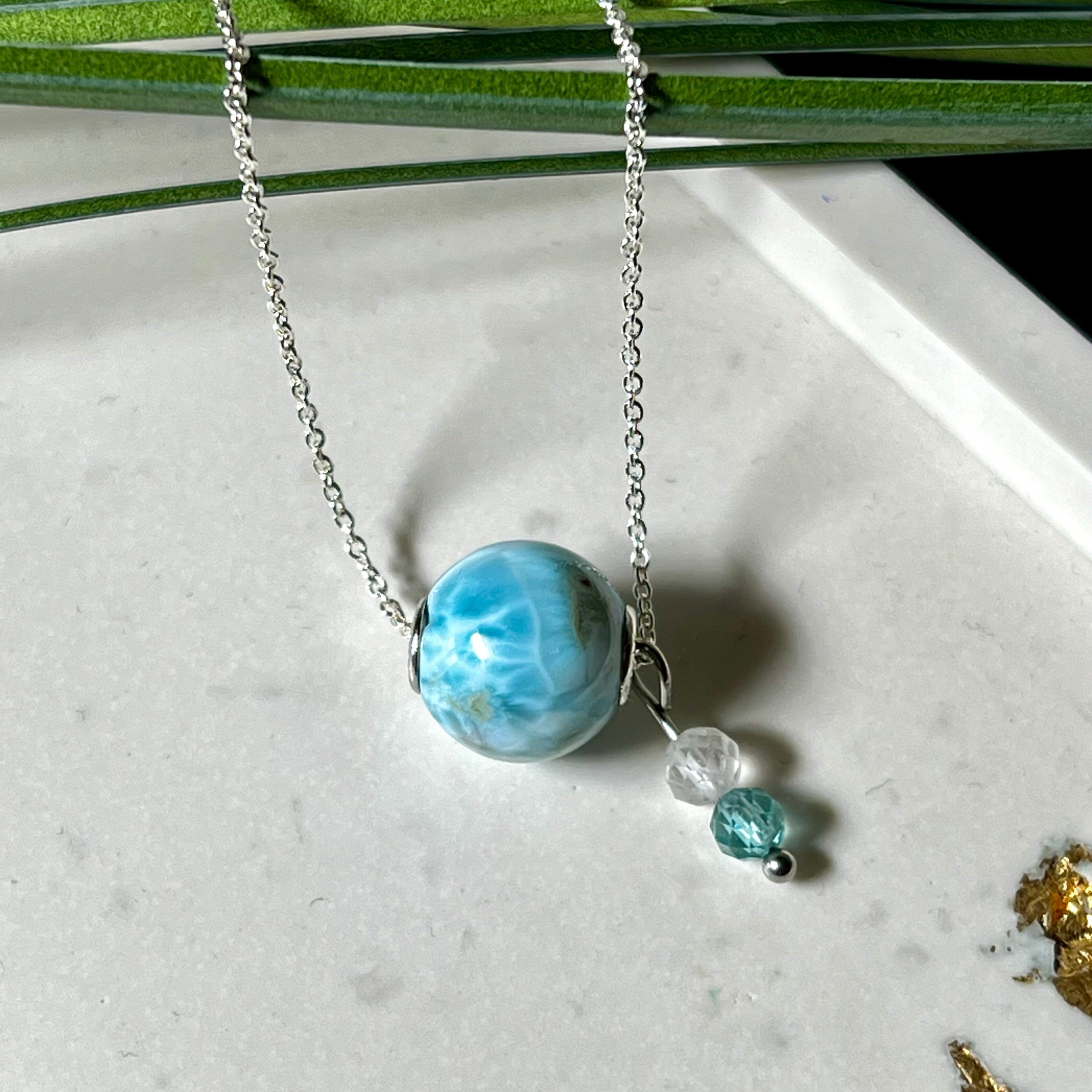 Feine Halskette aus 925er Silber mit einer polierten Larimar-Perle als Hauptstein, ergänzt durch funkelnde Apatit- und Bergkristall-Perlen. Der Edelstein mit seiner typischen Meeresfärbung erinnert an tropische Lagunen und steht für innere Ruhe und Klarheit.Ideal als Geschenk zum Geburtstag, für Meerliebhaber oder spirituelle Schmuckträgerinnen.