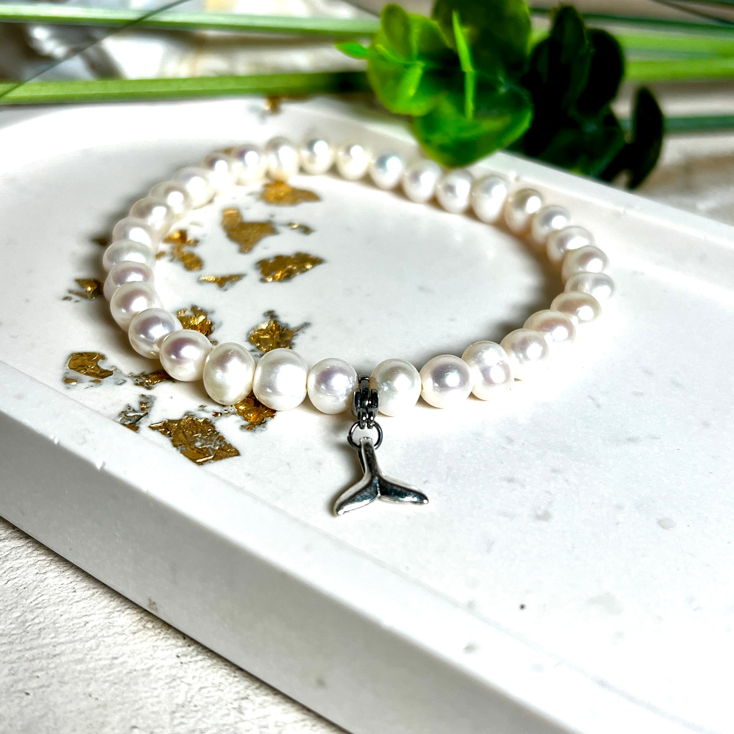 Handgefertigtes Armband aus echten Süßwasserperlen (ca. 6-7 mm), elastisch aufgezogen mit einem Edelstahl-Charm in Form einer Walflosse. Maritimes Design mit Bedeutung – stilvoll, natürlich und elegant. Größe ca. 17,5 cm. Ideal als Geschenk für Meeresliebhaberinnen oder für sich selbst.