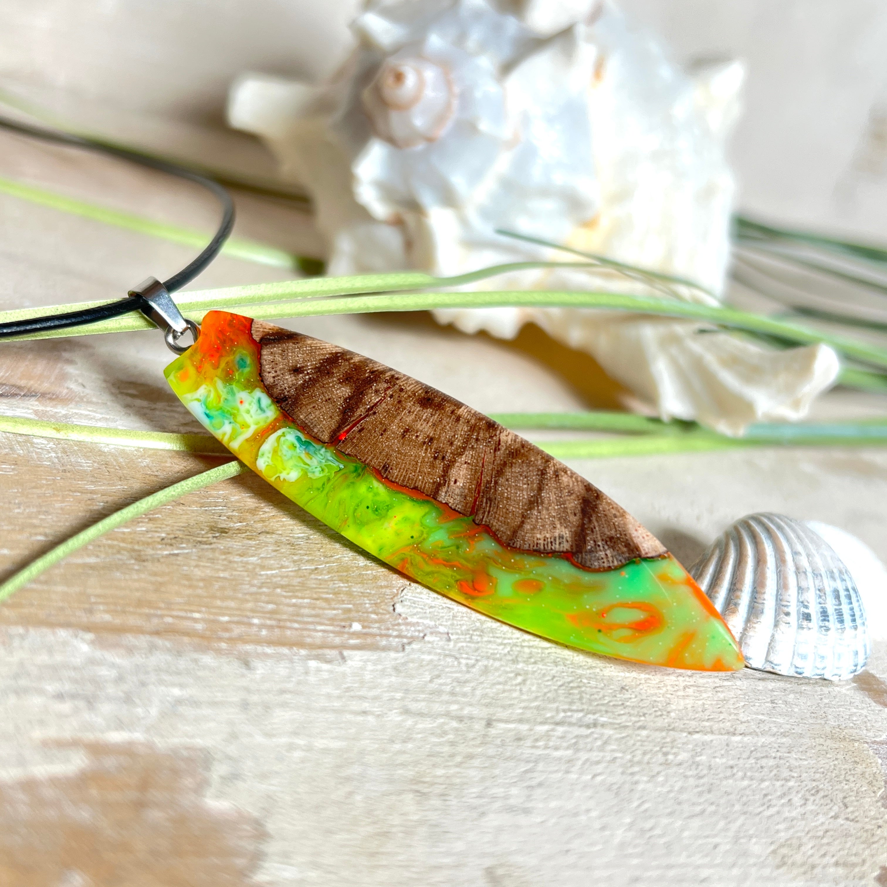 Handgefertigte Halskette „Tropical Glow“ mit Surfbrett-Anhänger aus naturbelassenem Rebholz (Weinrebe) und marmoriertem Epoxidharz in Grün, Orange, Türkis und Weiß. Größe des Anhängers ca. 6,5 × 2 cm. Das Harz fluoresziert eindrucksvoll unter UV-/Schwarzlicht. Edelstahl-Anhängerschlaufe, schwarze Lederkette (45 cm + 5 cm Verlängerung) mit Edelstahl-Karabiner. Unikat in maritim-sommerlichem Stil, ideal als besonderes Geschenk.